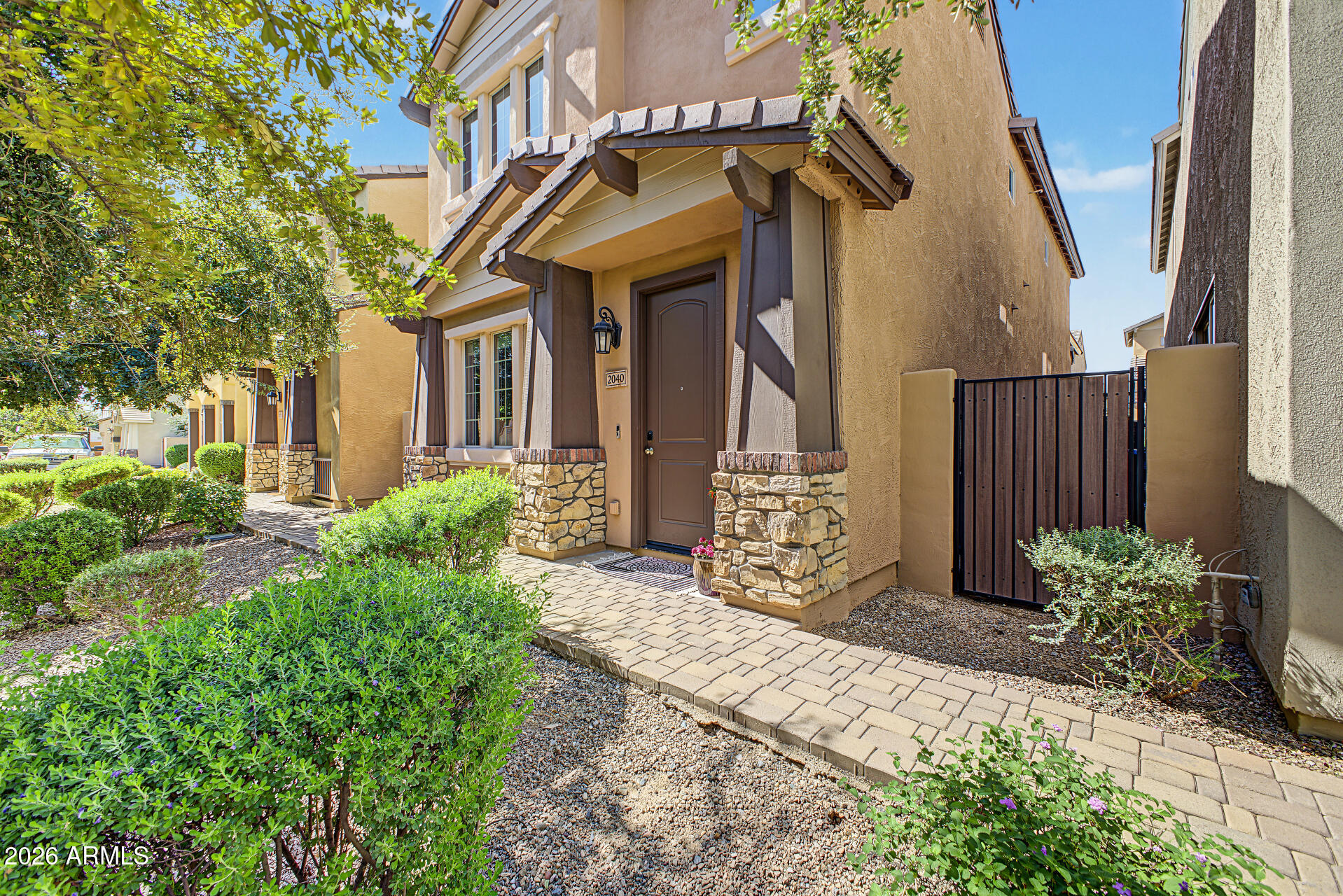 Front exterior with stone porch columns, landscaped walkway, and side gate.