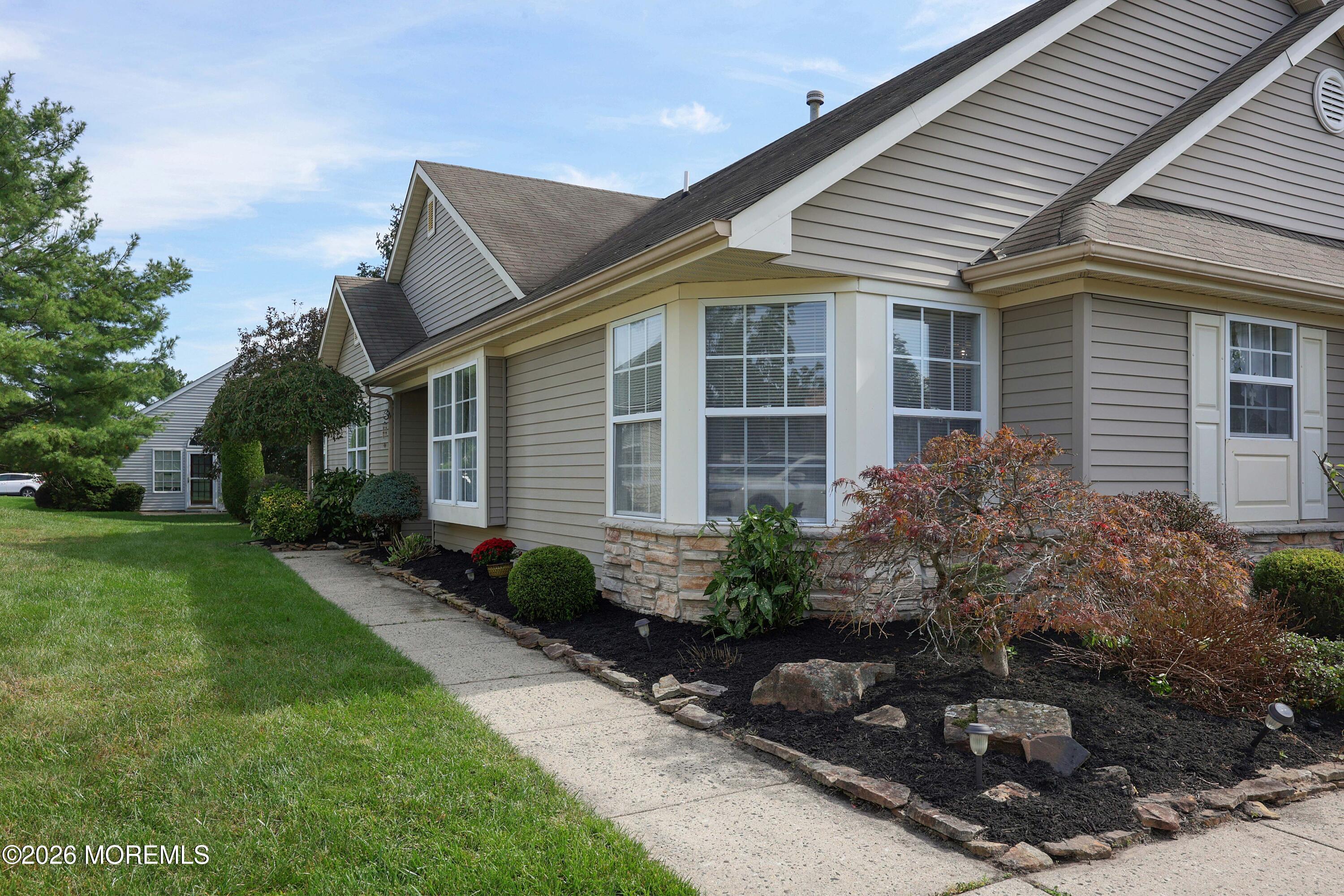 Gray-sided home with gabled roofs, white-trimmed windows, landscaped beds, and a curved walkway.