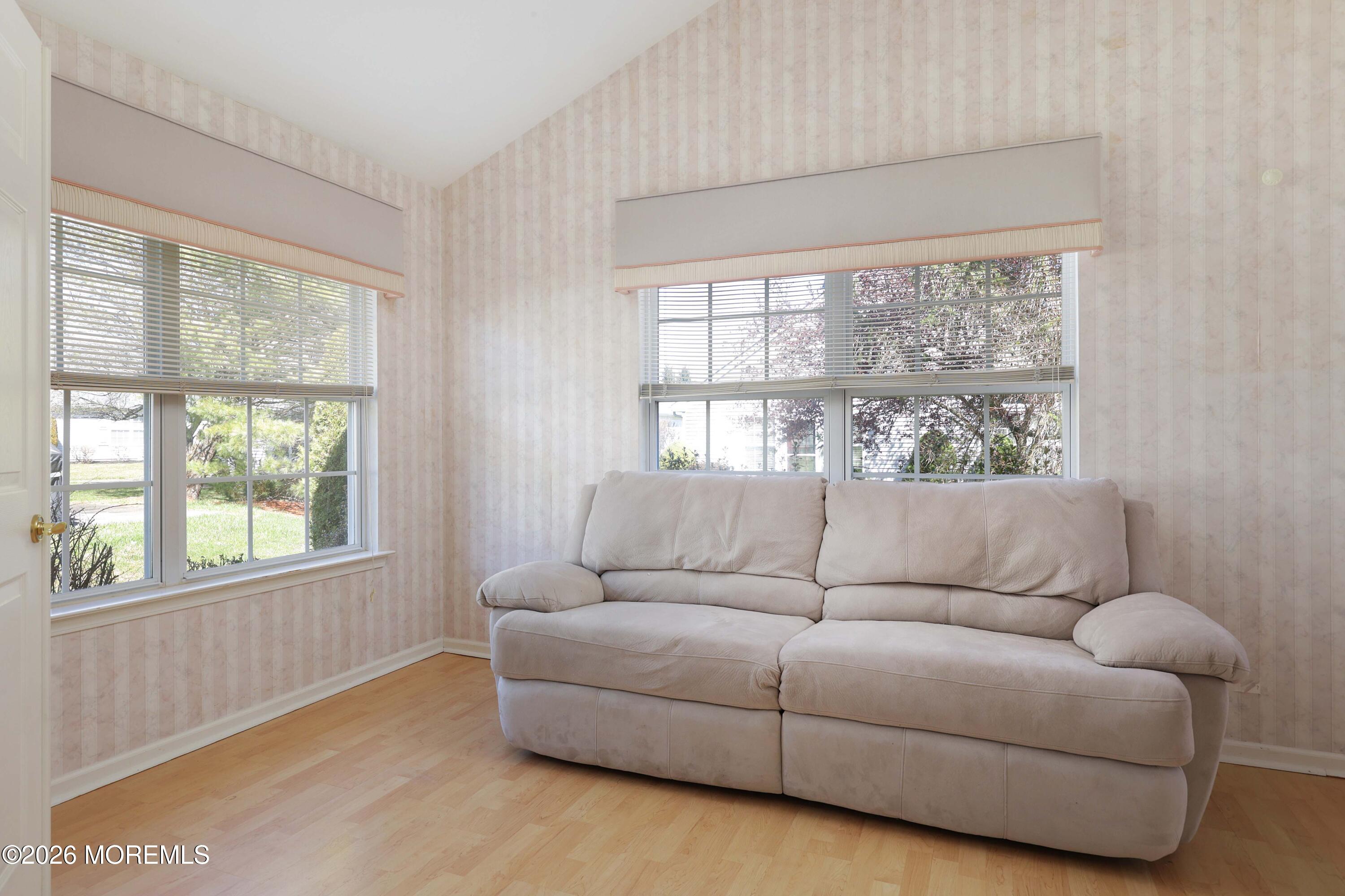 Living room with a large beige sectional sofa, pale striped wallpaper, and two wide windows.