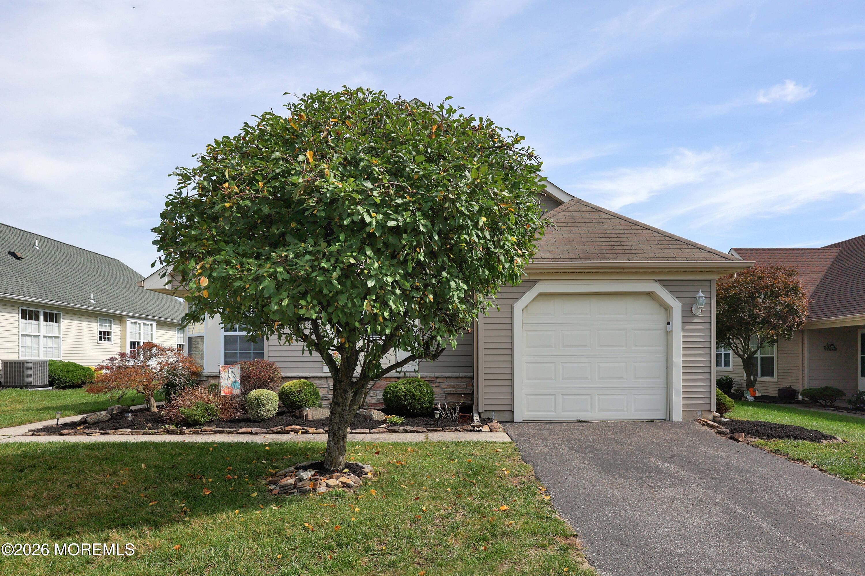 Beige home with a white garage door, partly screened by a large tree.