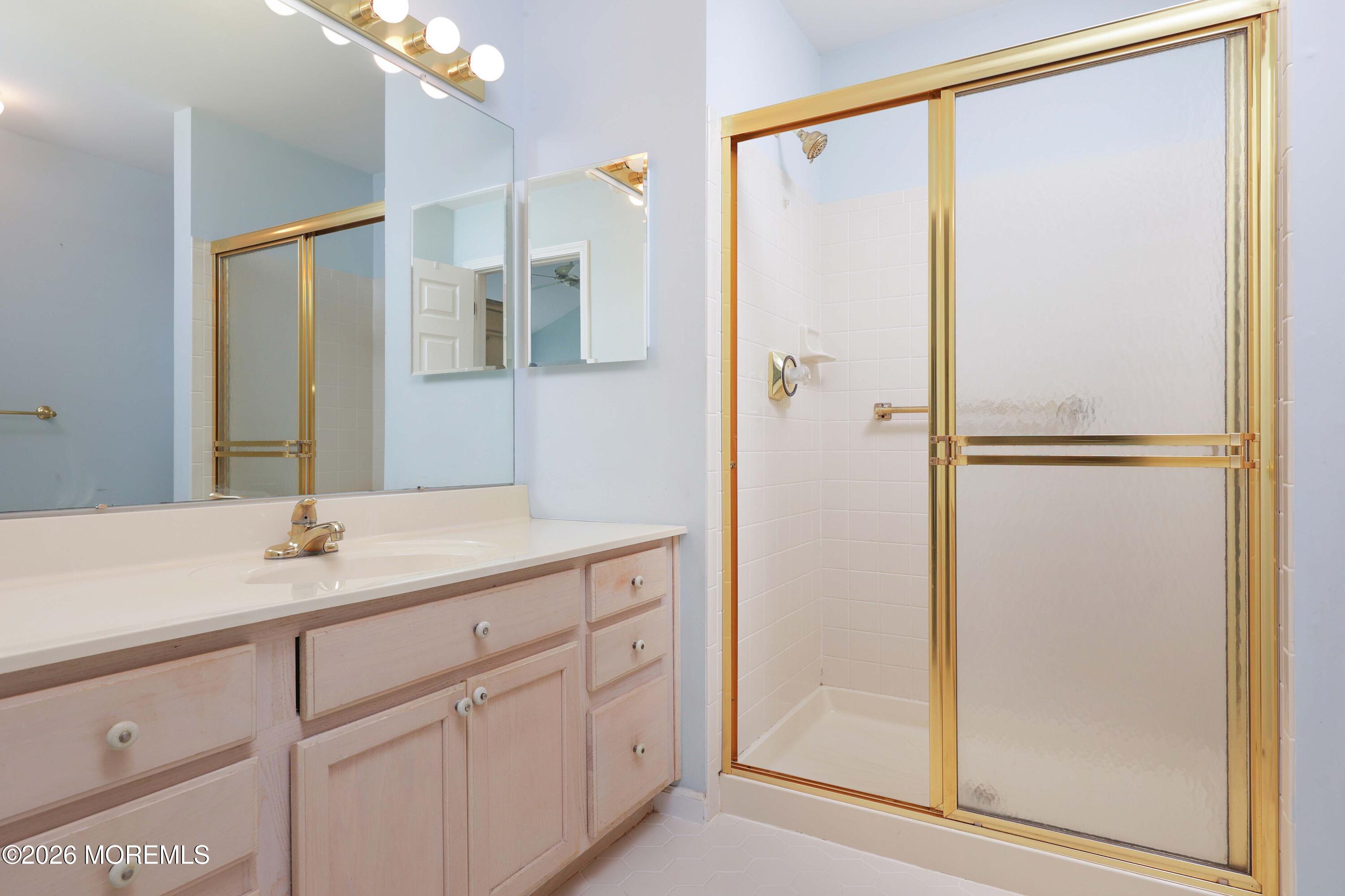 Bathroom with a pale wood vanity and gold-framed frosted-glass shower.