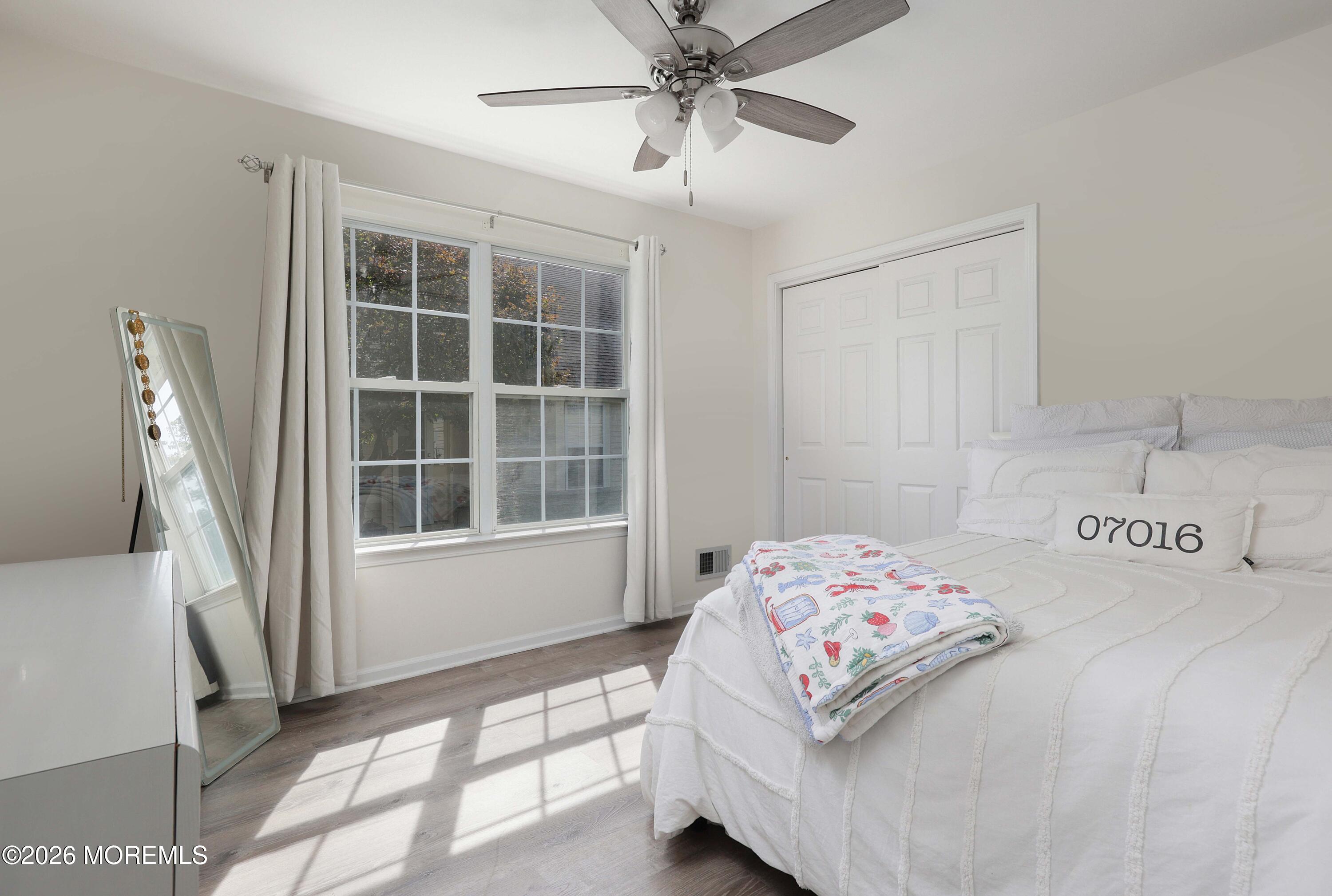 Bright bedroom with a white bed, colorful folded blanket, and large curtained windows.