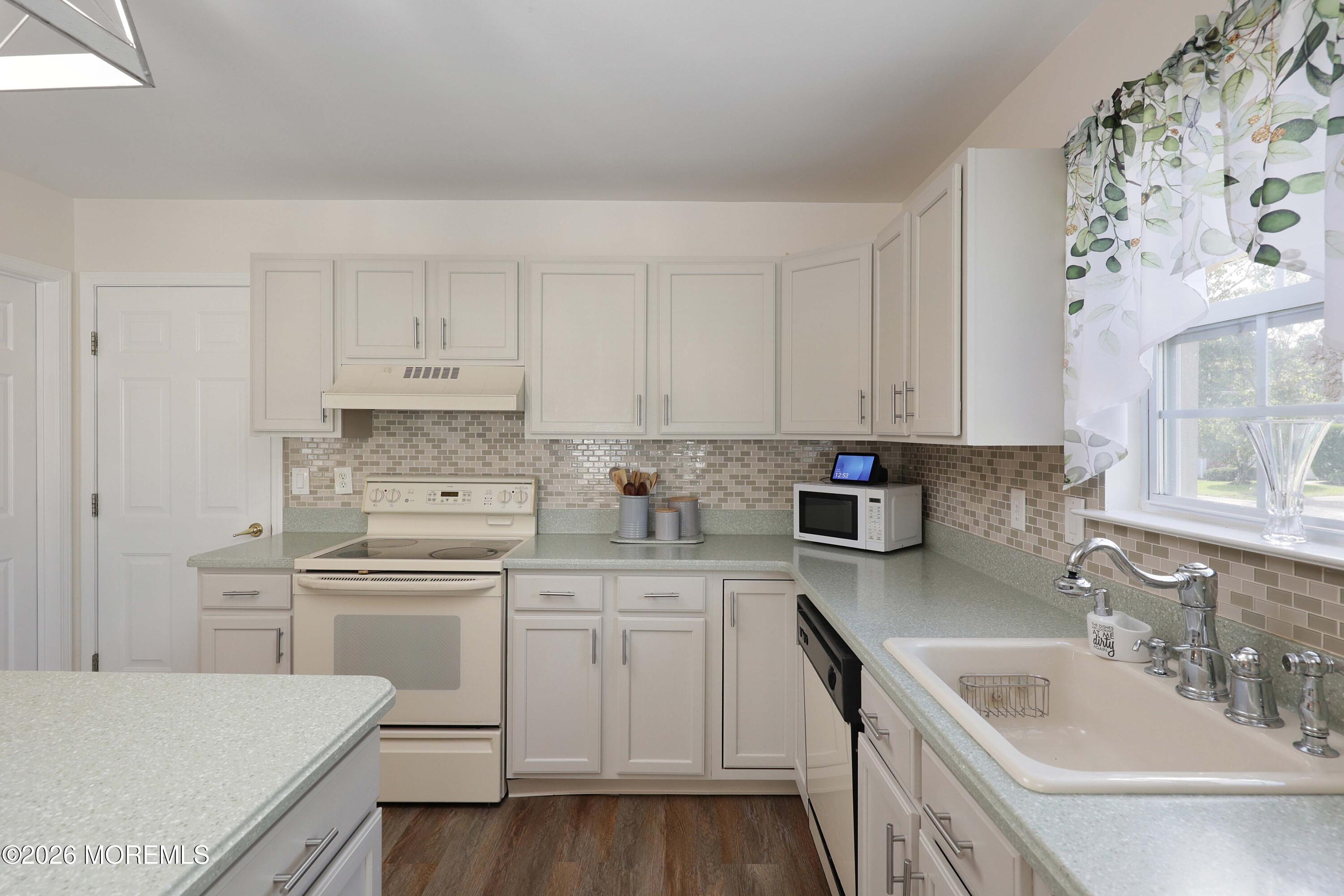 Kitchen with white cabinets, pale green counters, tiled backsplash, and a large sink beneath a window.