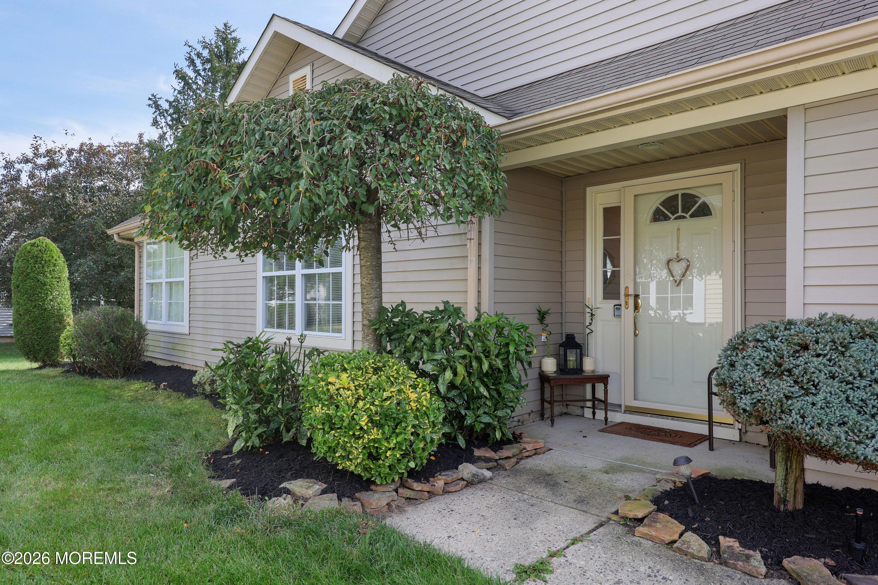 Home entrance with a white glass-paneled door, covered porch, and landscaped shrubs.