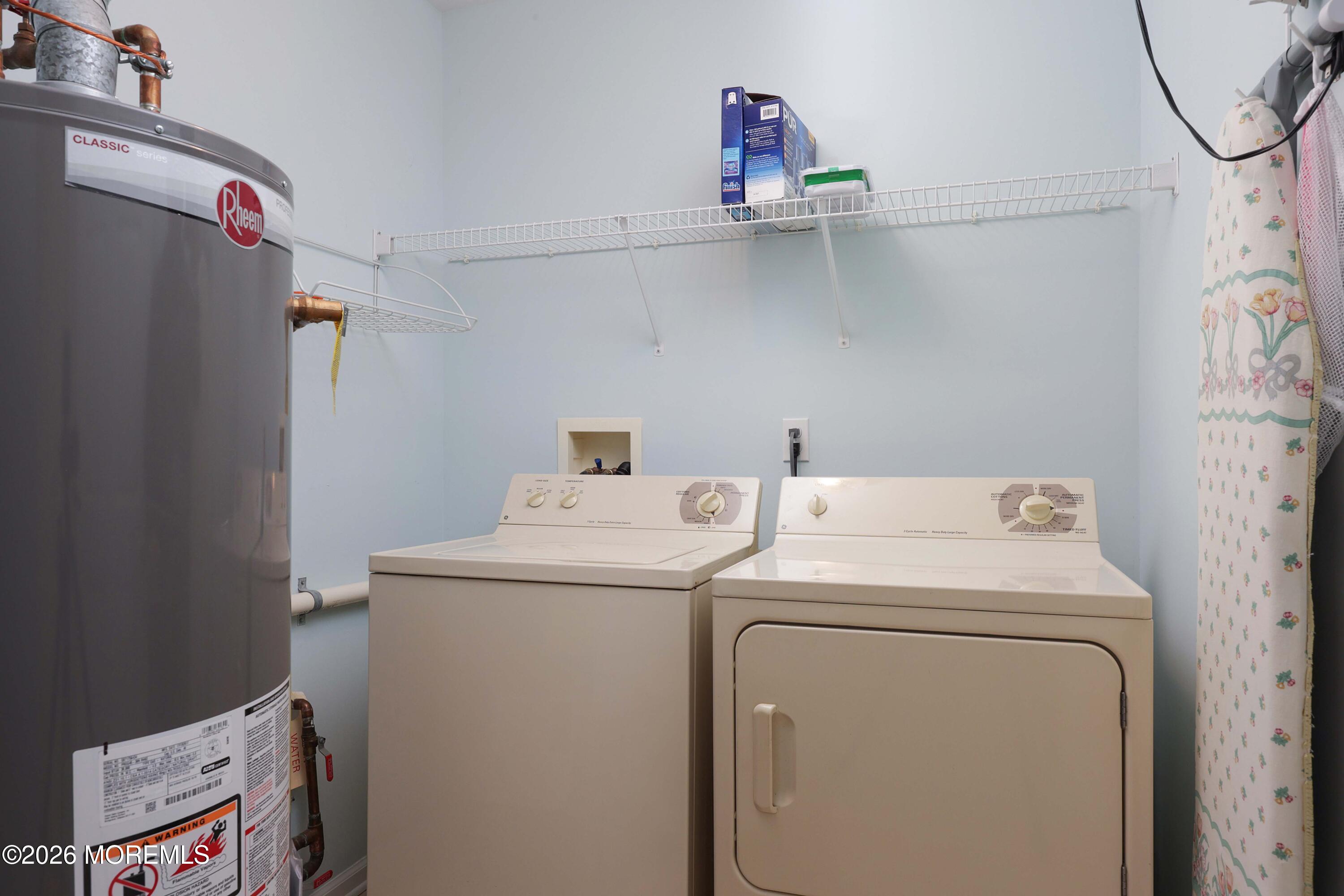 Laundry room with a washer, dryer, wire shelves, and a large water heater.