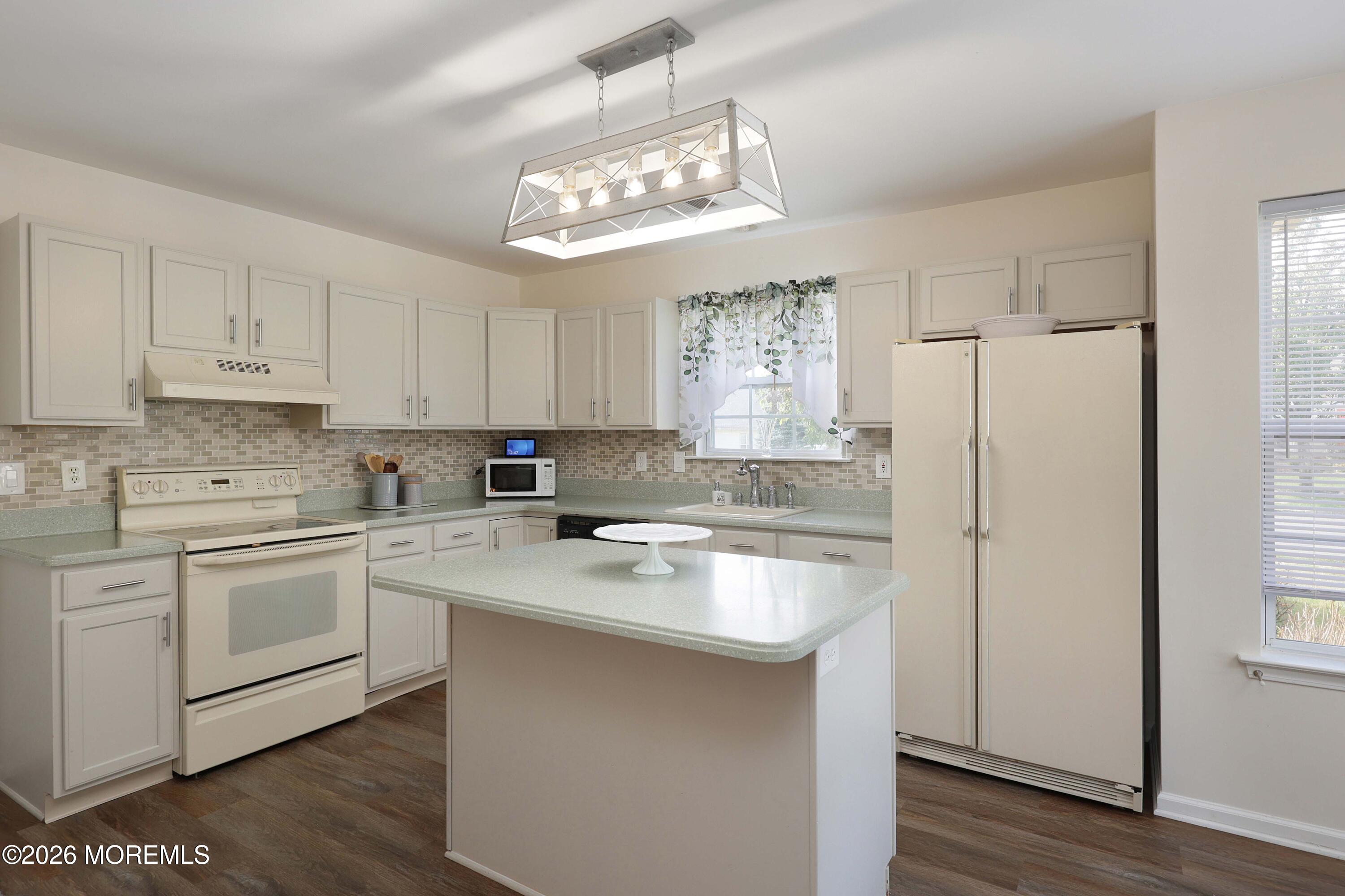 Kitchen with cream cabinets, a central island, tiled backsplash, and window above the sink.