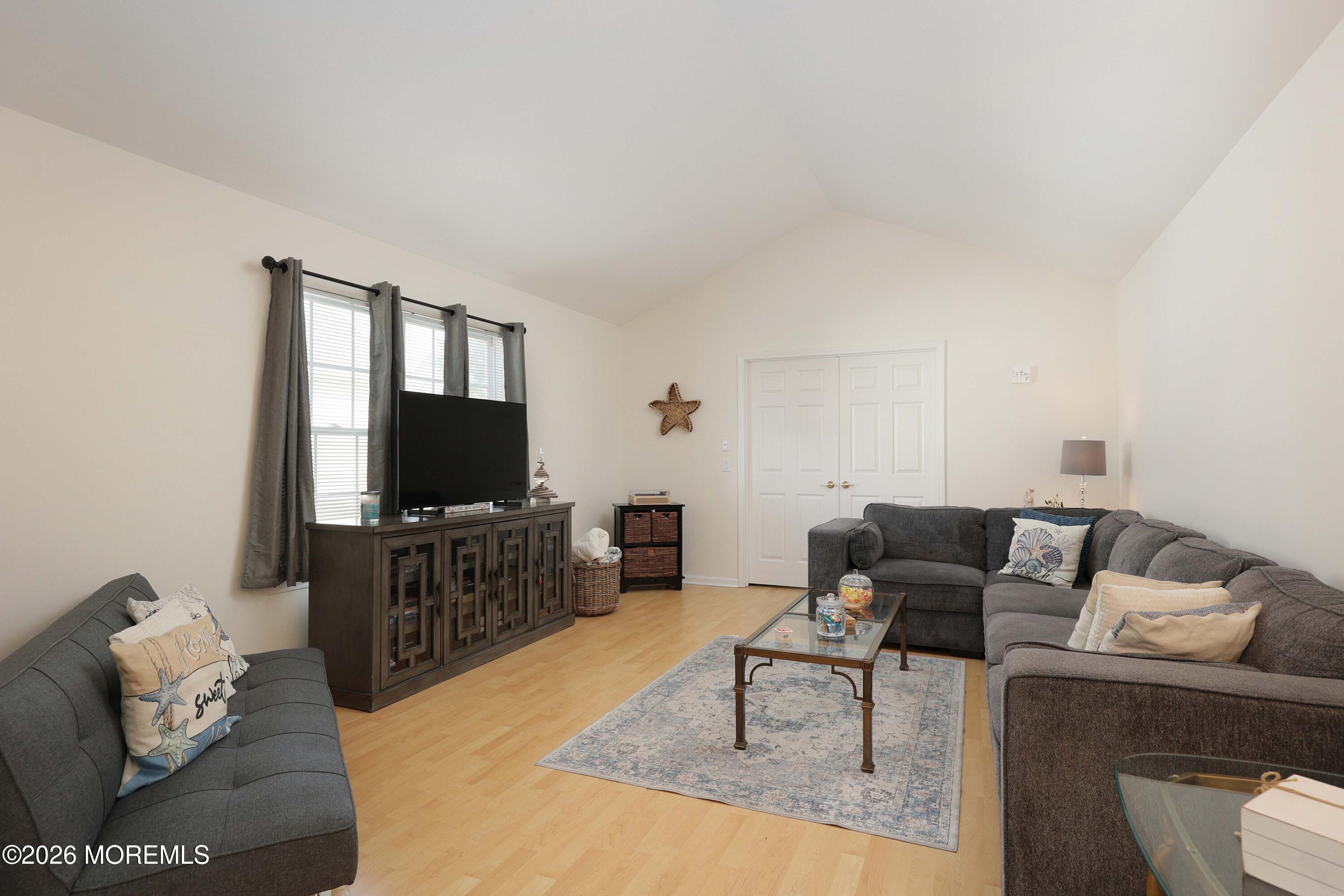 Furnished living room with gray sectional sofas, a television, and a patterned rug on pale wood flooring.