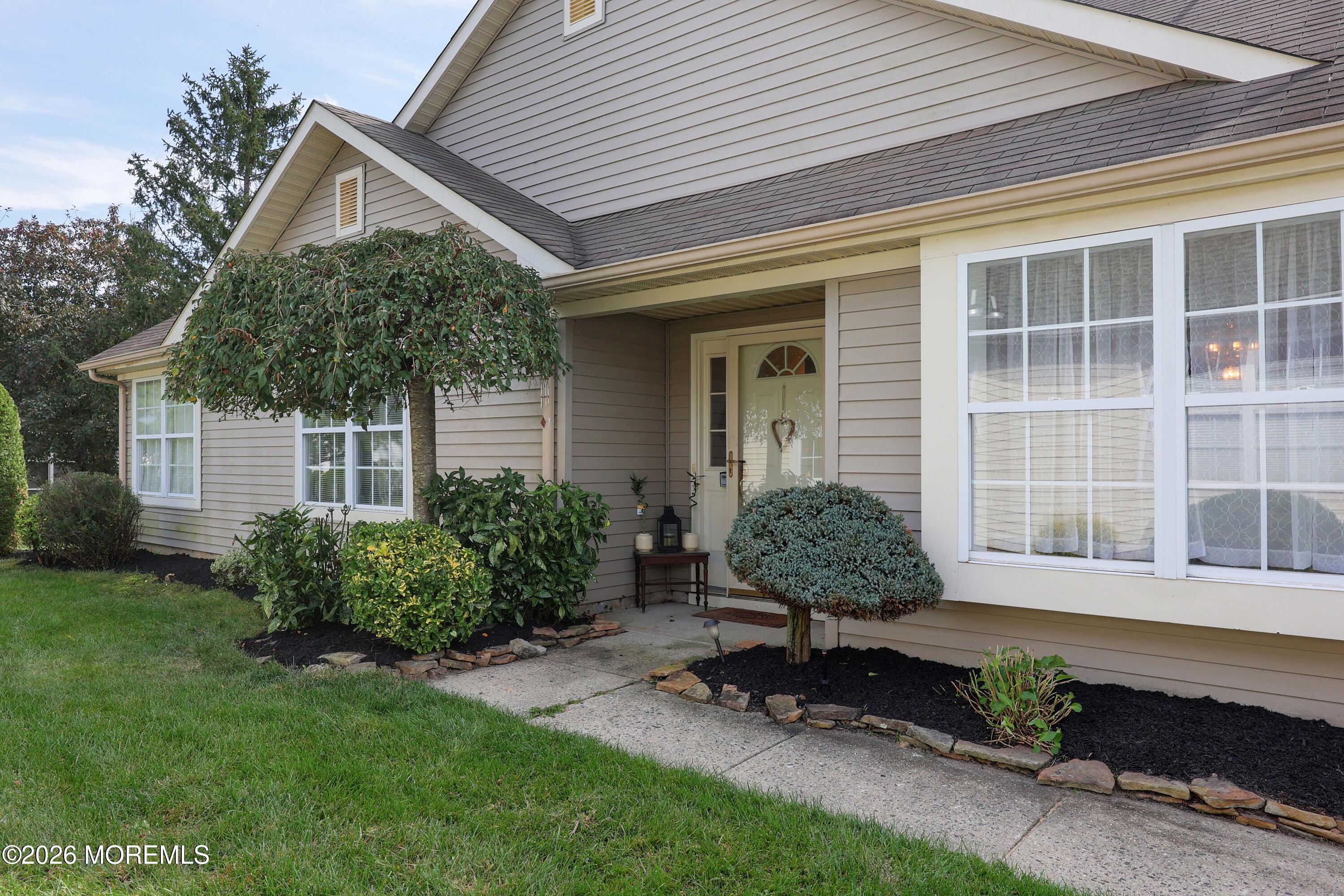 Beige-sided home with a covered entry, landscaped shrubs, and a concrete walkway.