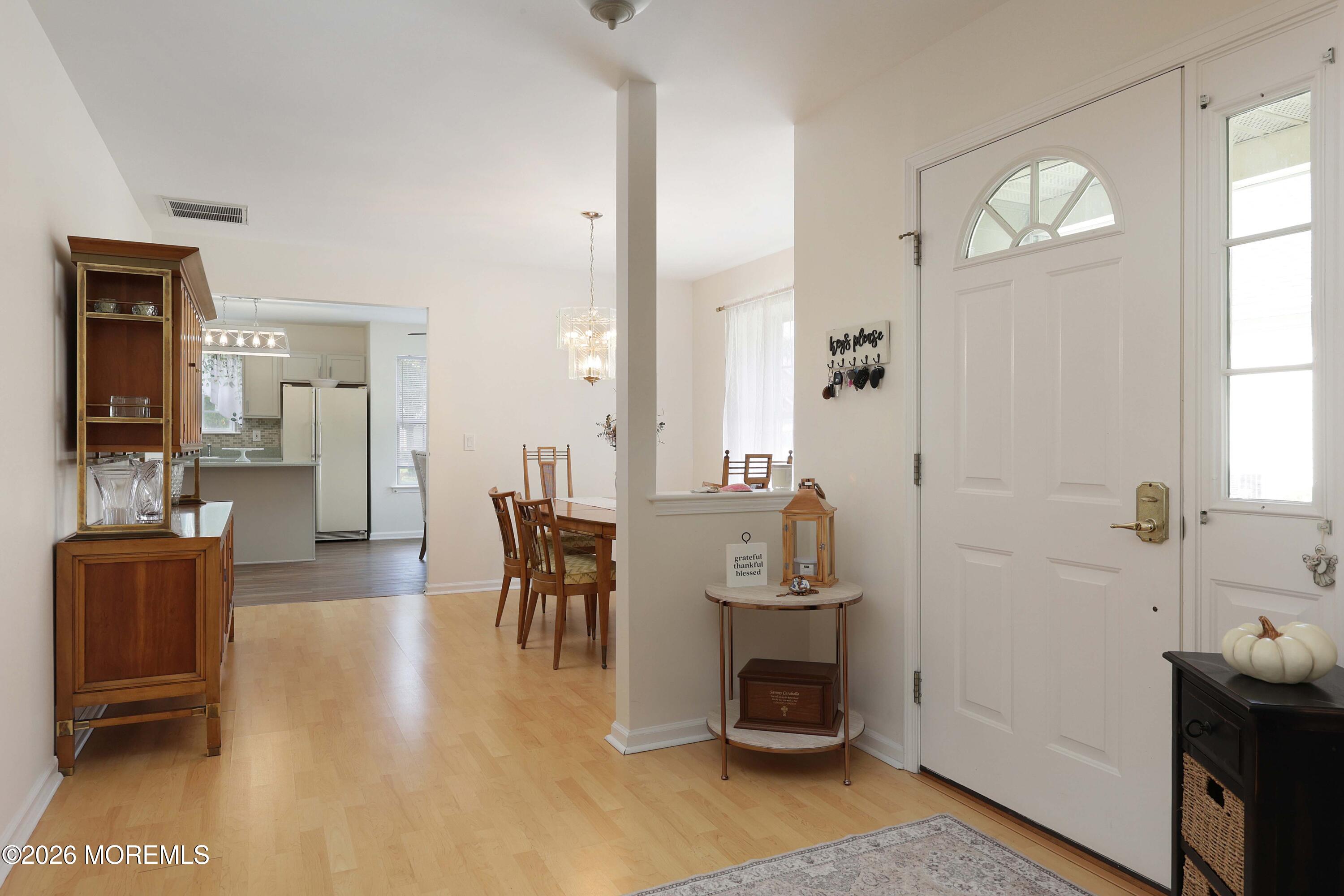 Entry foyer with a white front door, hardwood flooring, and a dining area opening to the kitchen.