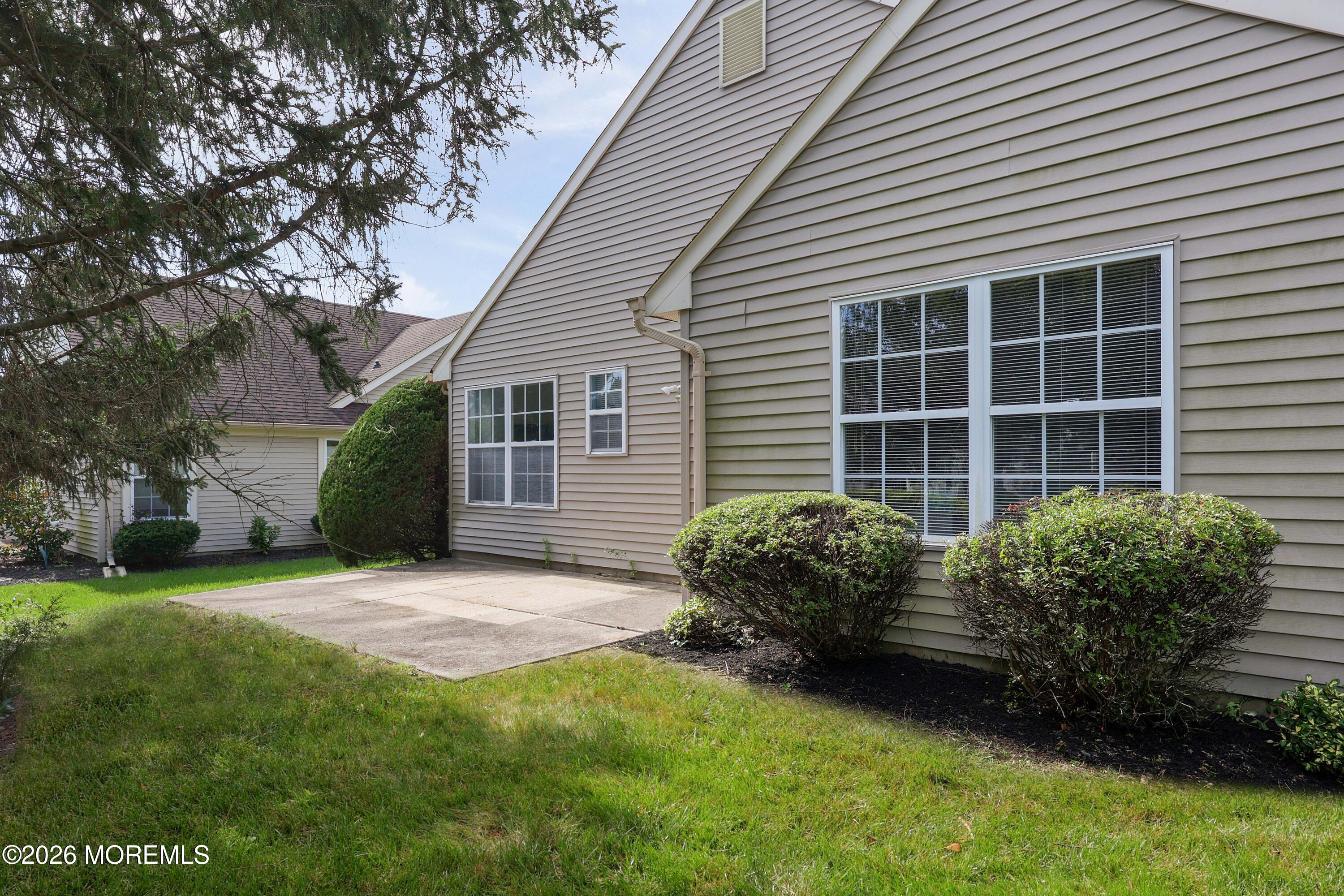 House exterior with a concrete patio, large windows, trimmed shrubs, and lawn.