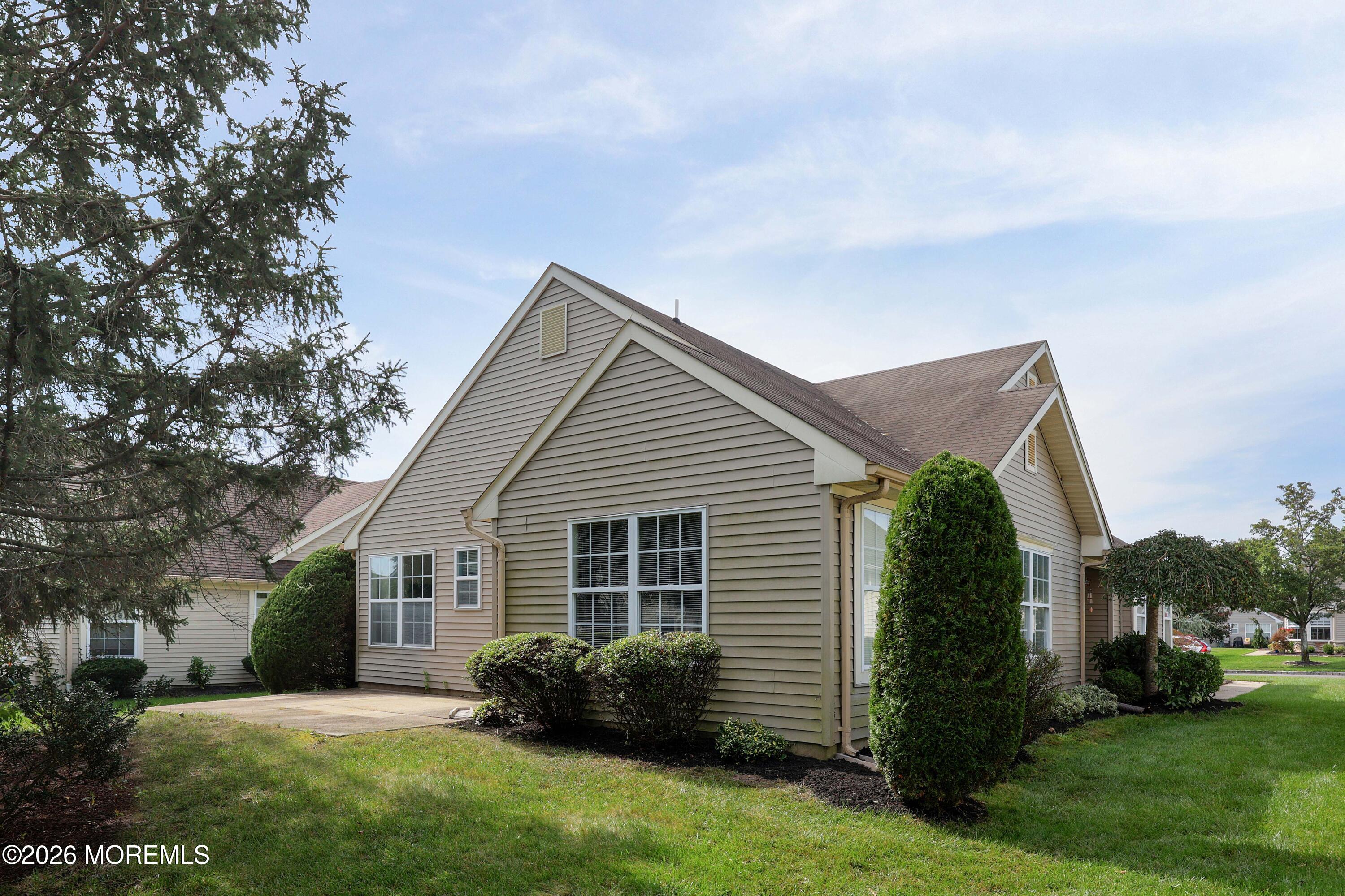 Beige two-story home with a multi-gabled roof, concrete patio, and landscaped lawn.