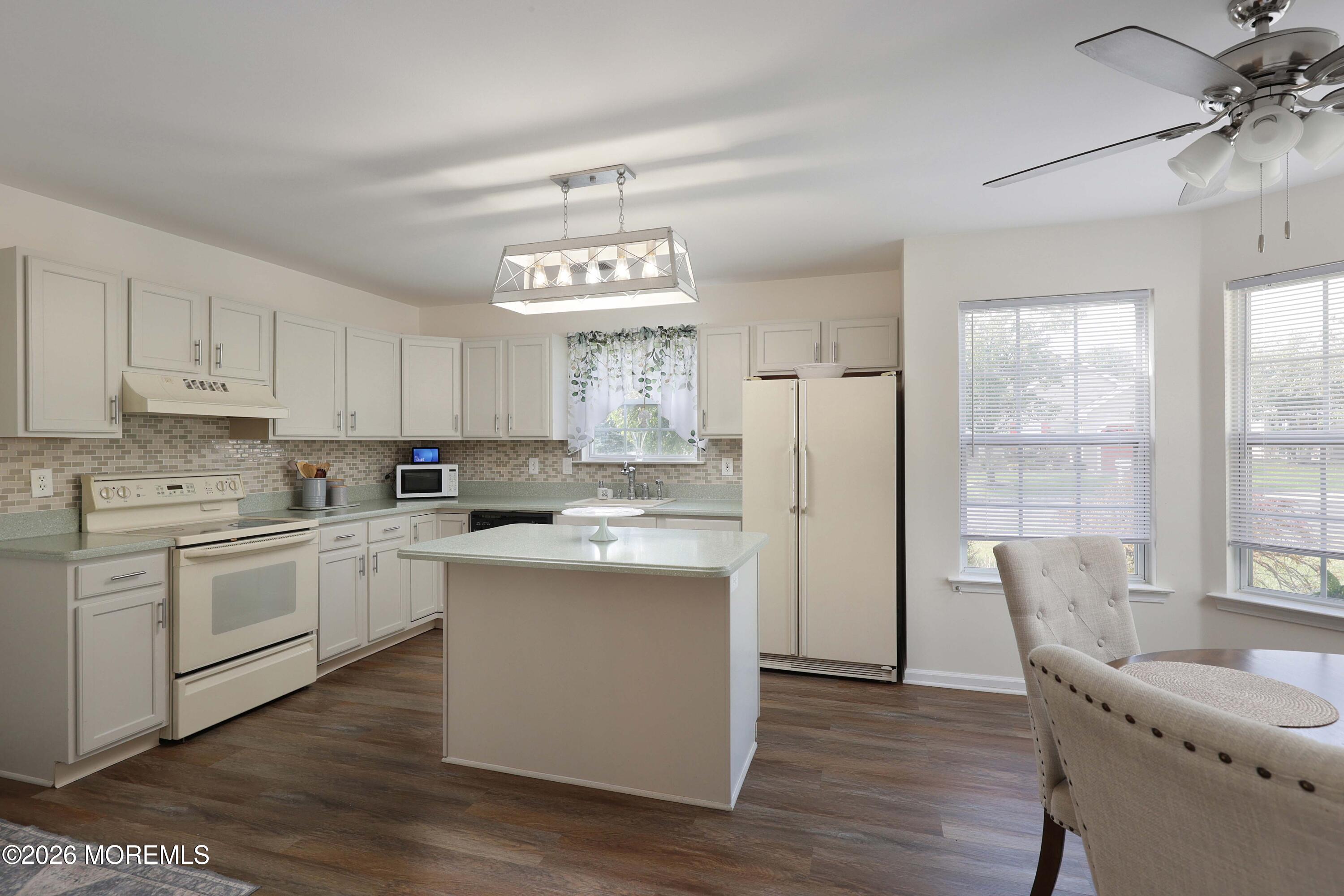 Kitchen with white cabinetry, central island, tiled backsplash, and dining area beside large windows.