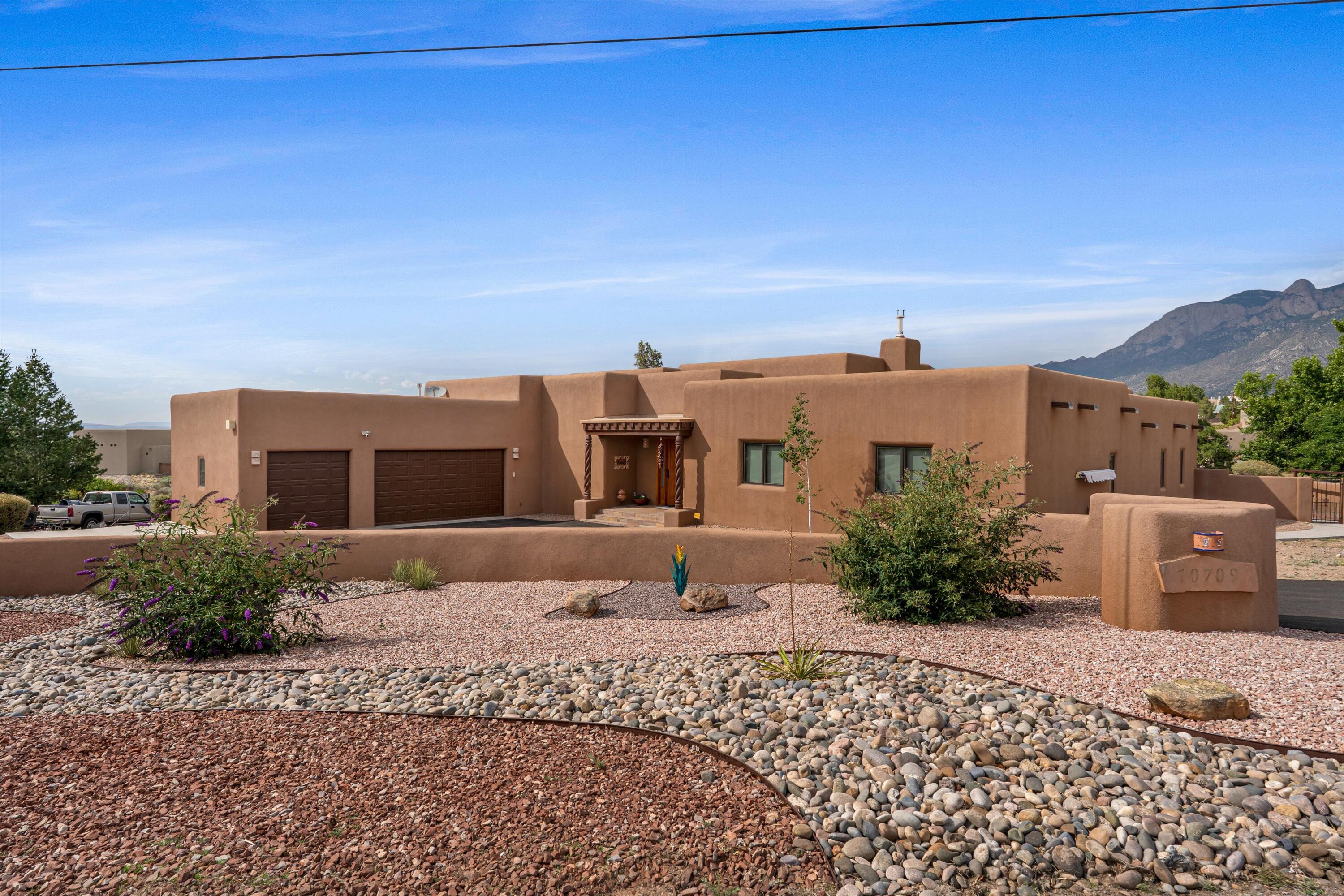 Adobe-style home with two garage doors, gravel landscaping, and mountains behind it.