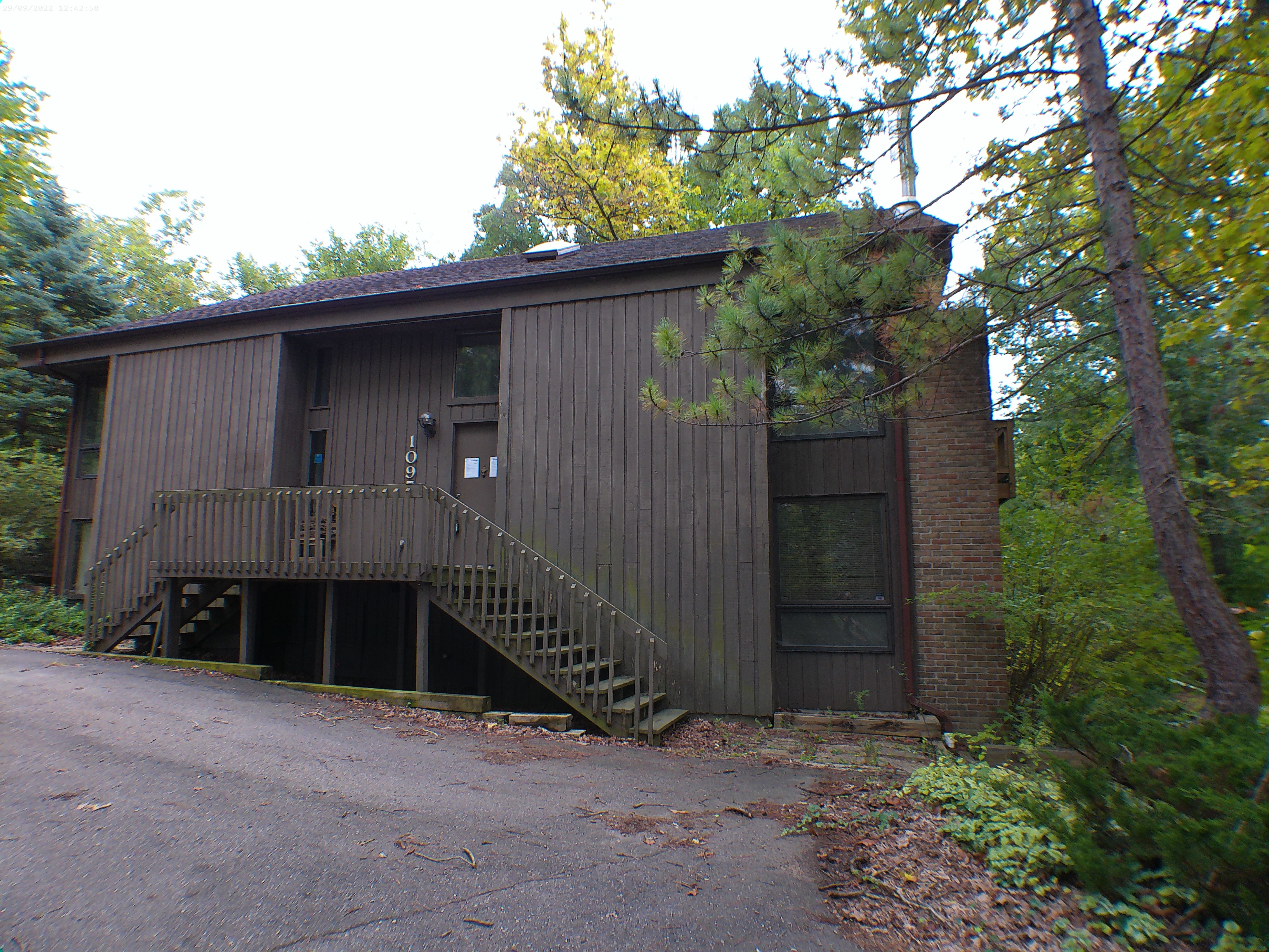 Wooded house with brown siding, a brick section, and a raised entry deck with stairs.