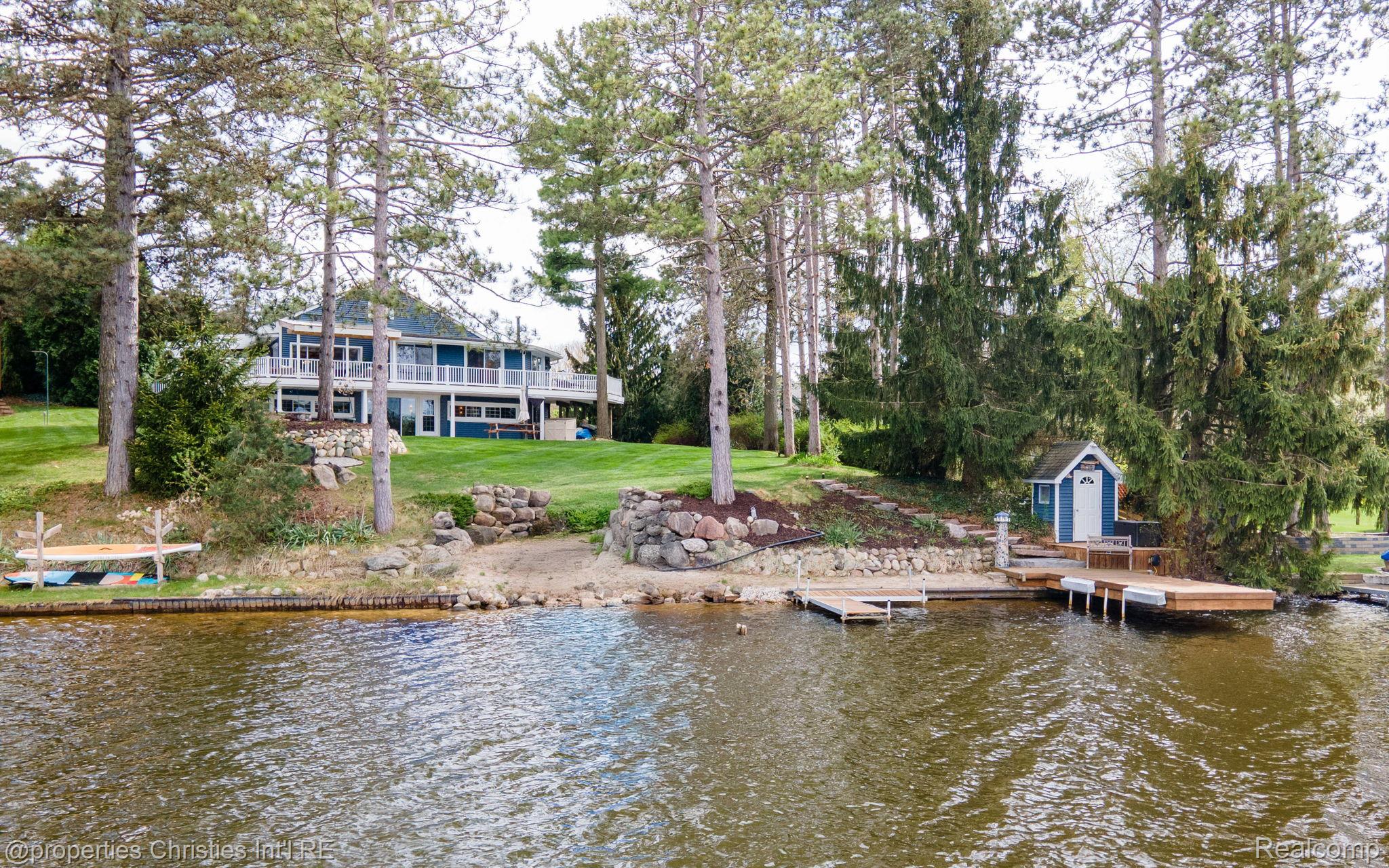 Lakefront home with a blue exterior, tree-lined lawn, stone landscaping, and private docks.