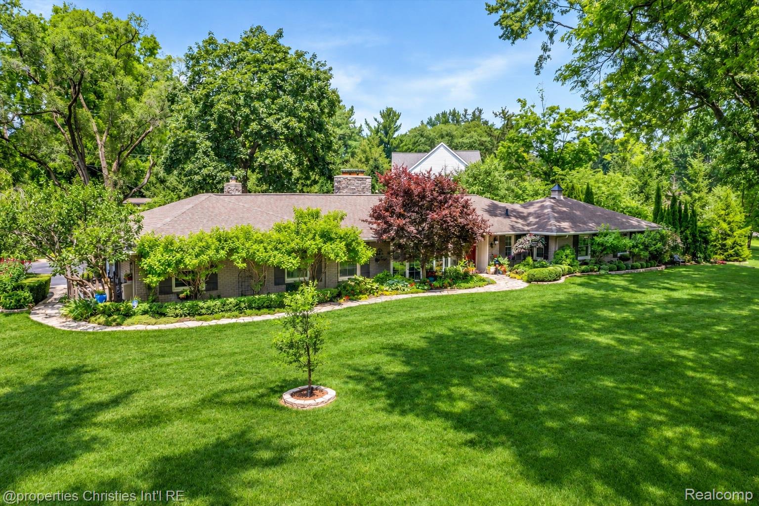 Single-story home surrounded by mature trees, landscaped gardens, and a broad green lawn.