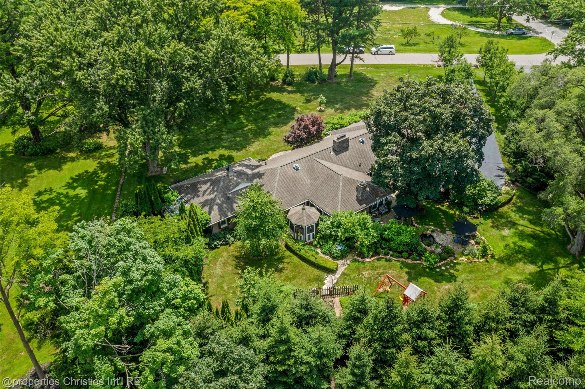 Aerial view of a tree-surrounded home with landscaped grounds, gazebo, and backyard swing set.