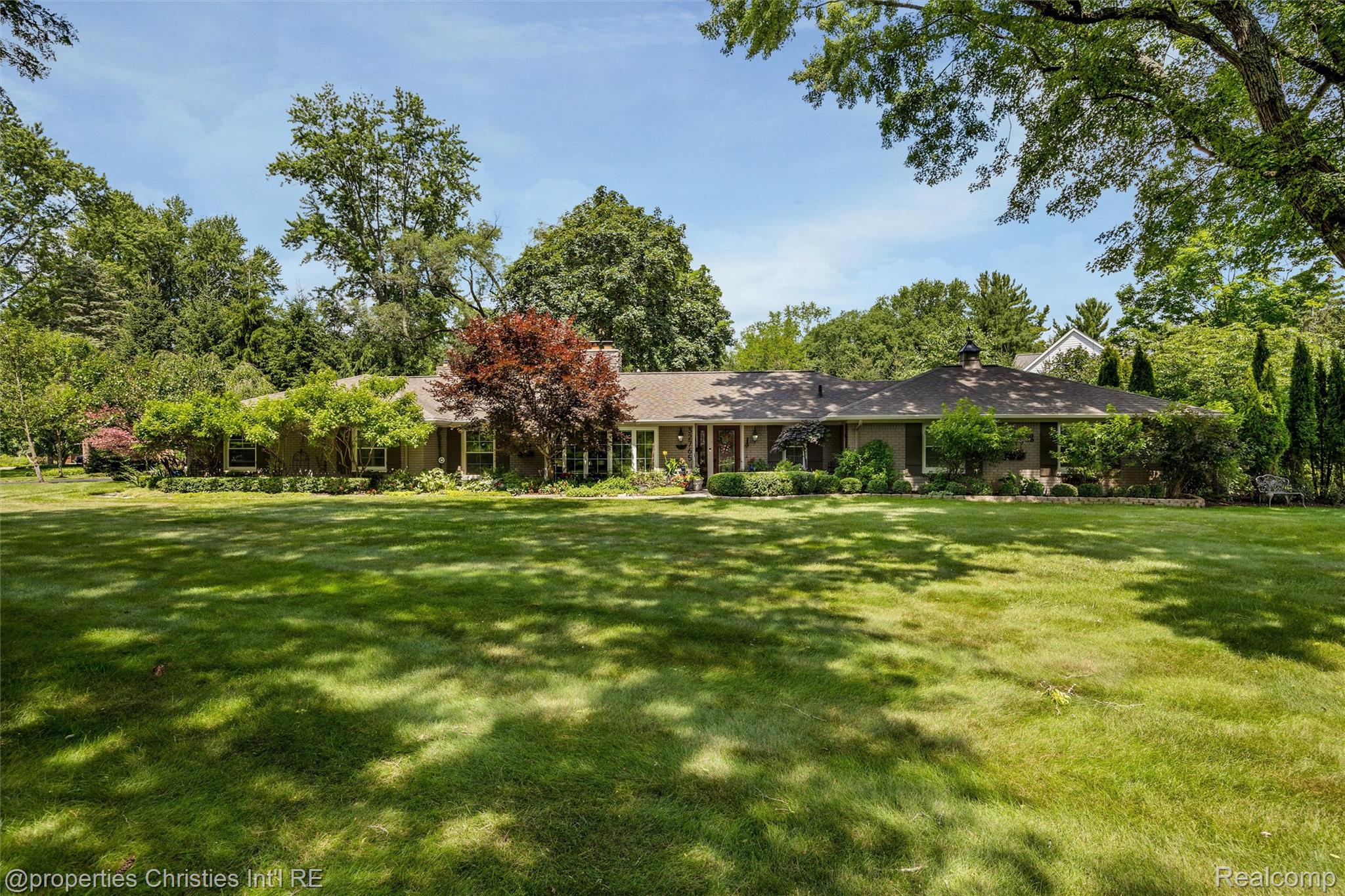 Single-story brick home set behind a broad lawn and mature trees.