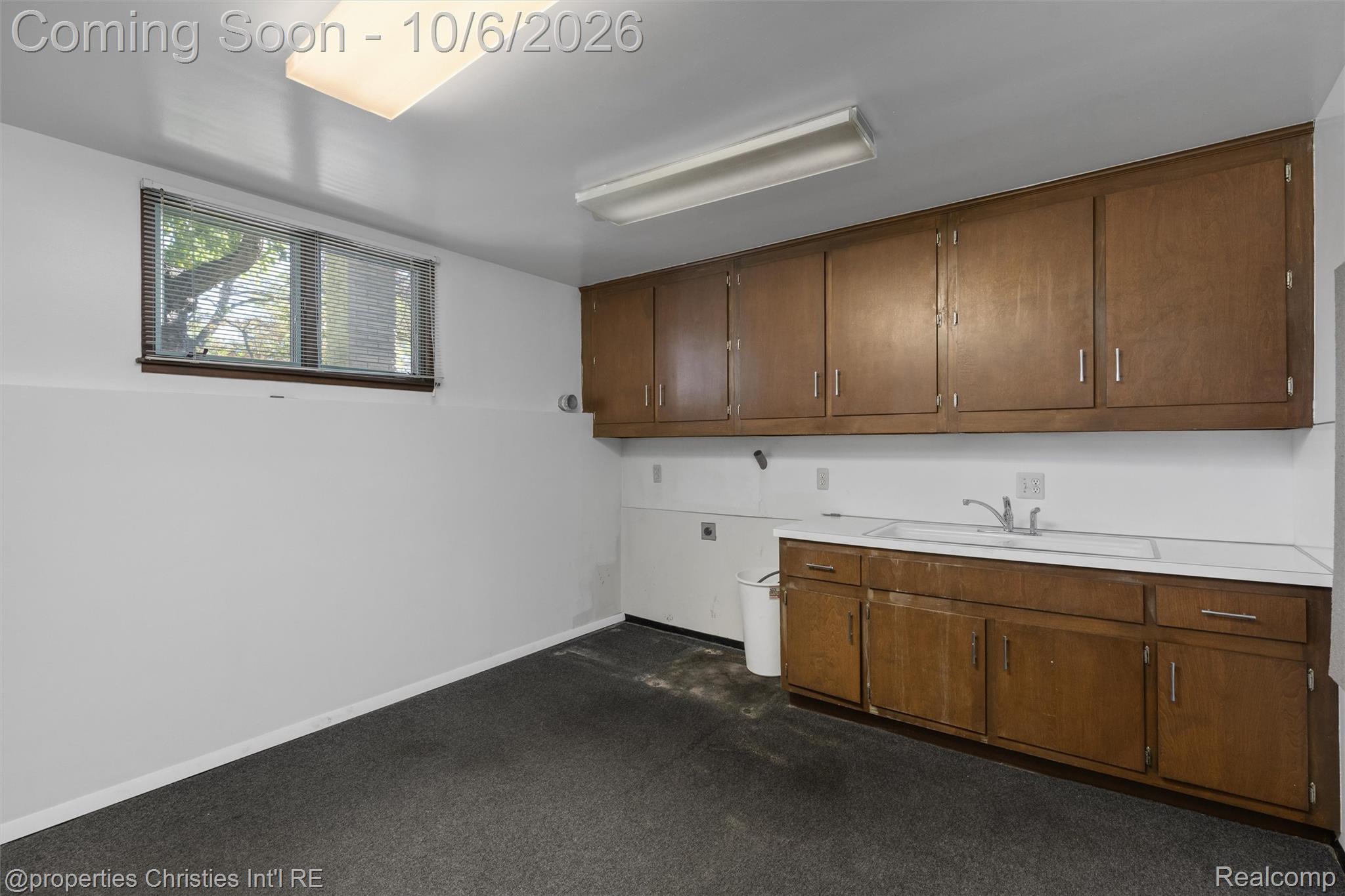 Utility room with extensive wood cabinetry, a built-in sink, and a window with blinds.