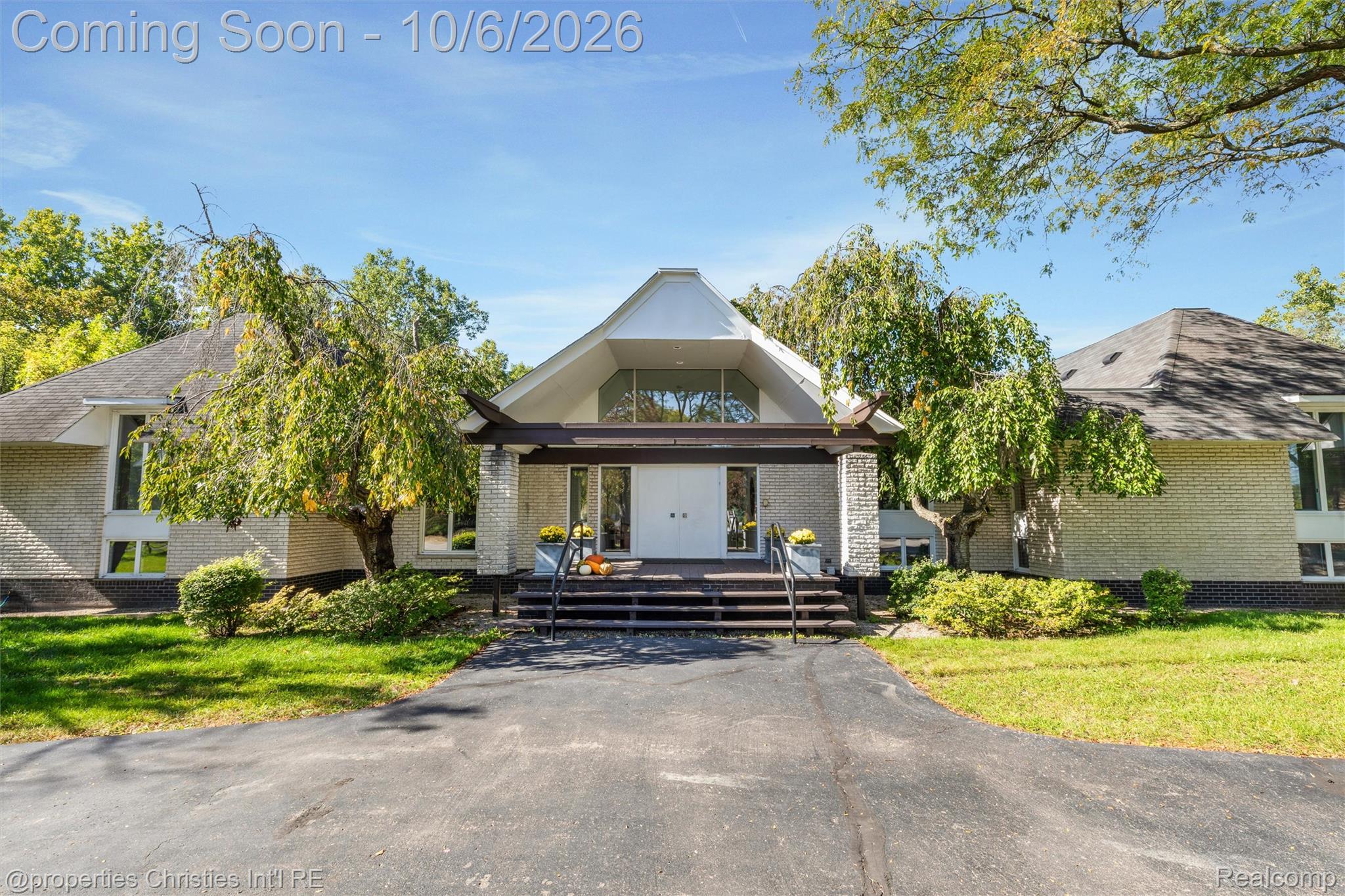 Brick home with a distinctive peaked entry, front steps, and broad asphalt driveway.