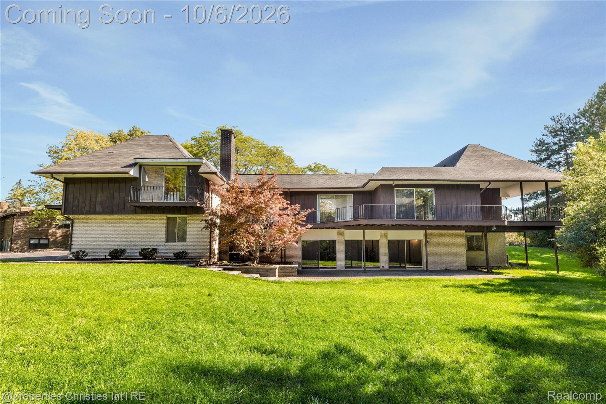 Rear of a two-story house with broad balconies overlooking a large lawn.