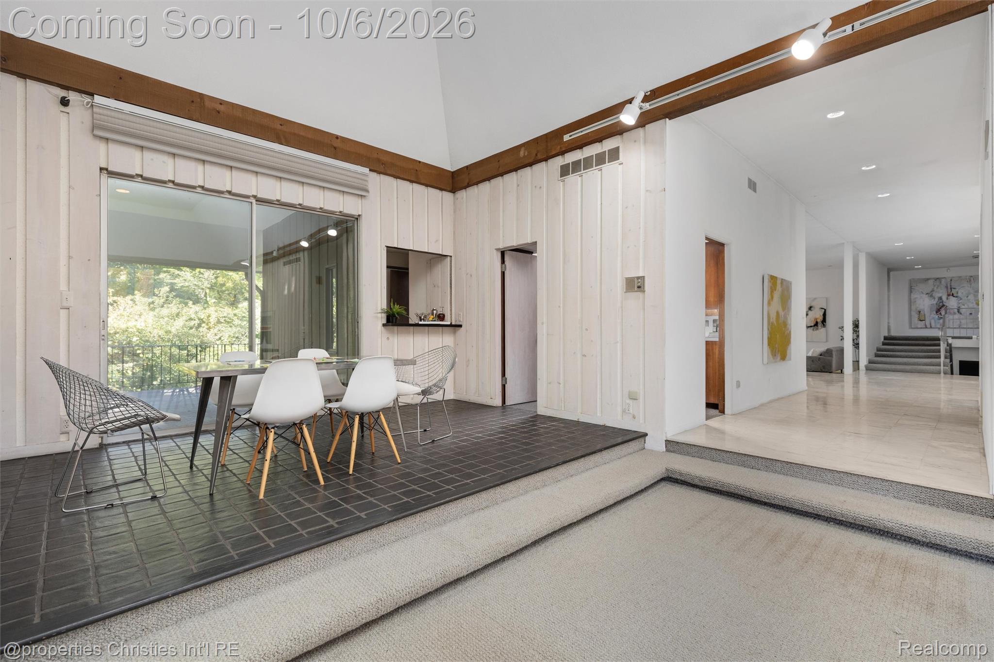 Dining area with a glass table and sliding doors, opening toward a bright hallway.