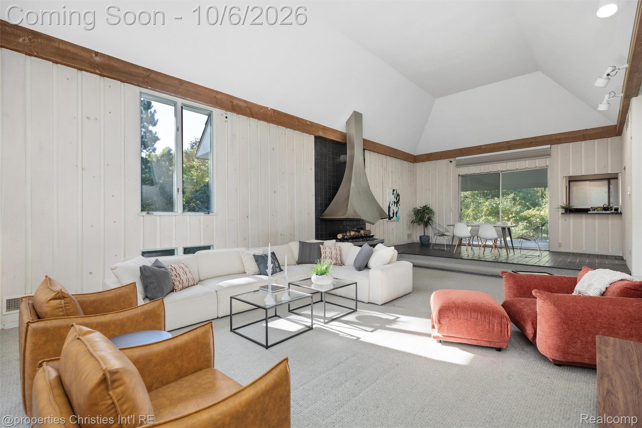 Living room with vaulted ceiling, sculptural fireplace, white sectional, and raised dining area.
