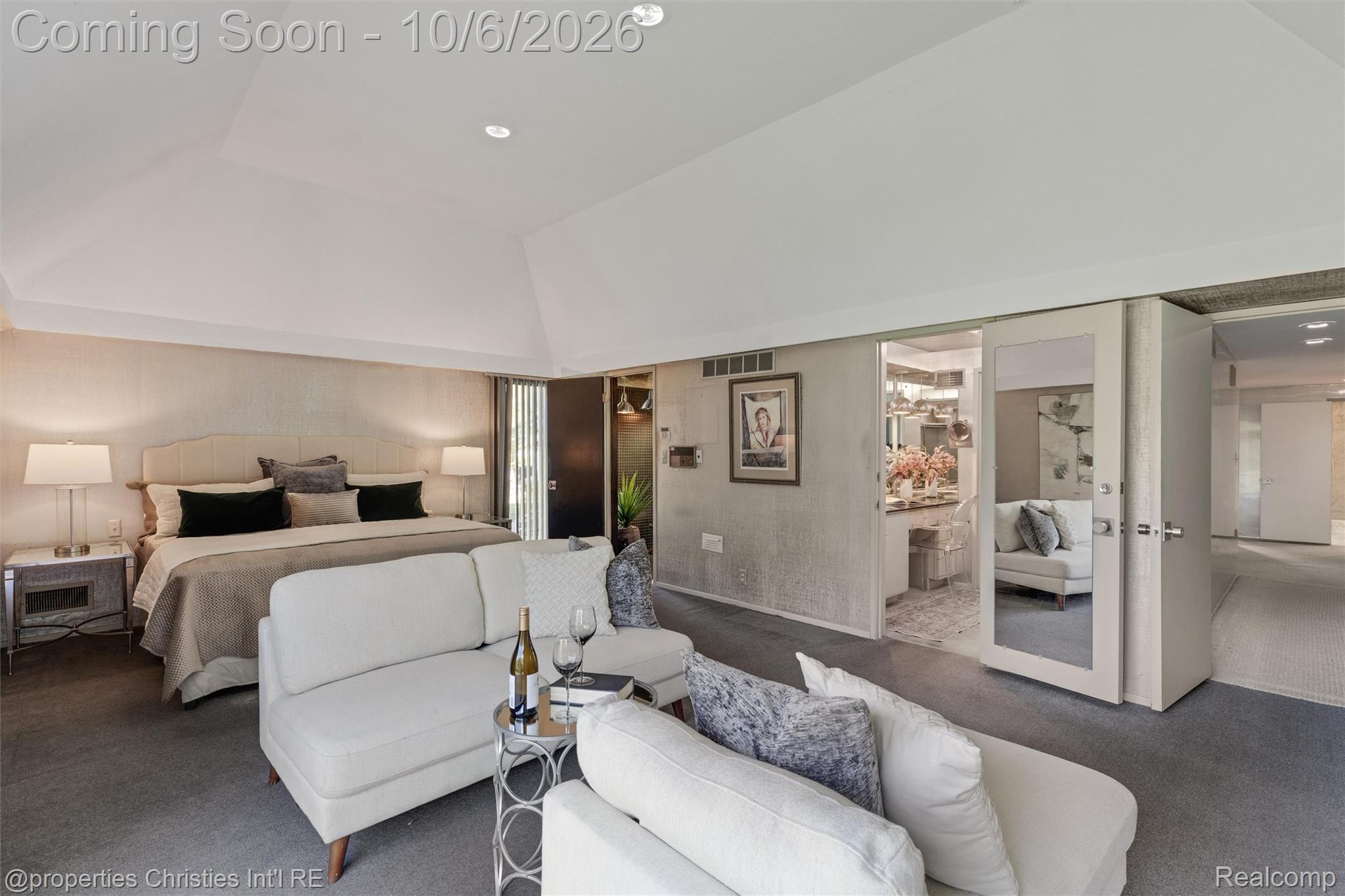 Staged bedroom with a large bed, white sectional sofas, and open doors to adjoining rooms.