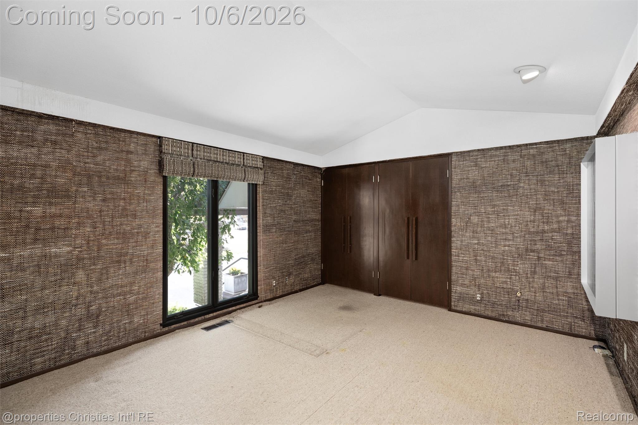 Empty bedroom with woven brown walls, a dark wood closet, and a sliding glass door.