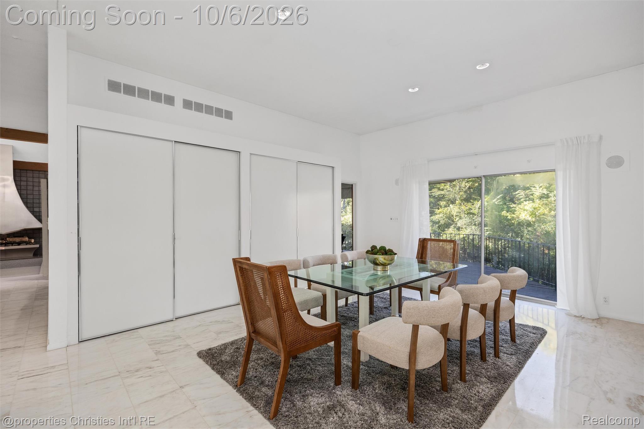 Dining room with glass table, cane-back chairs, and sliding doors opening to a wooded balcony.