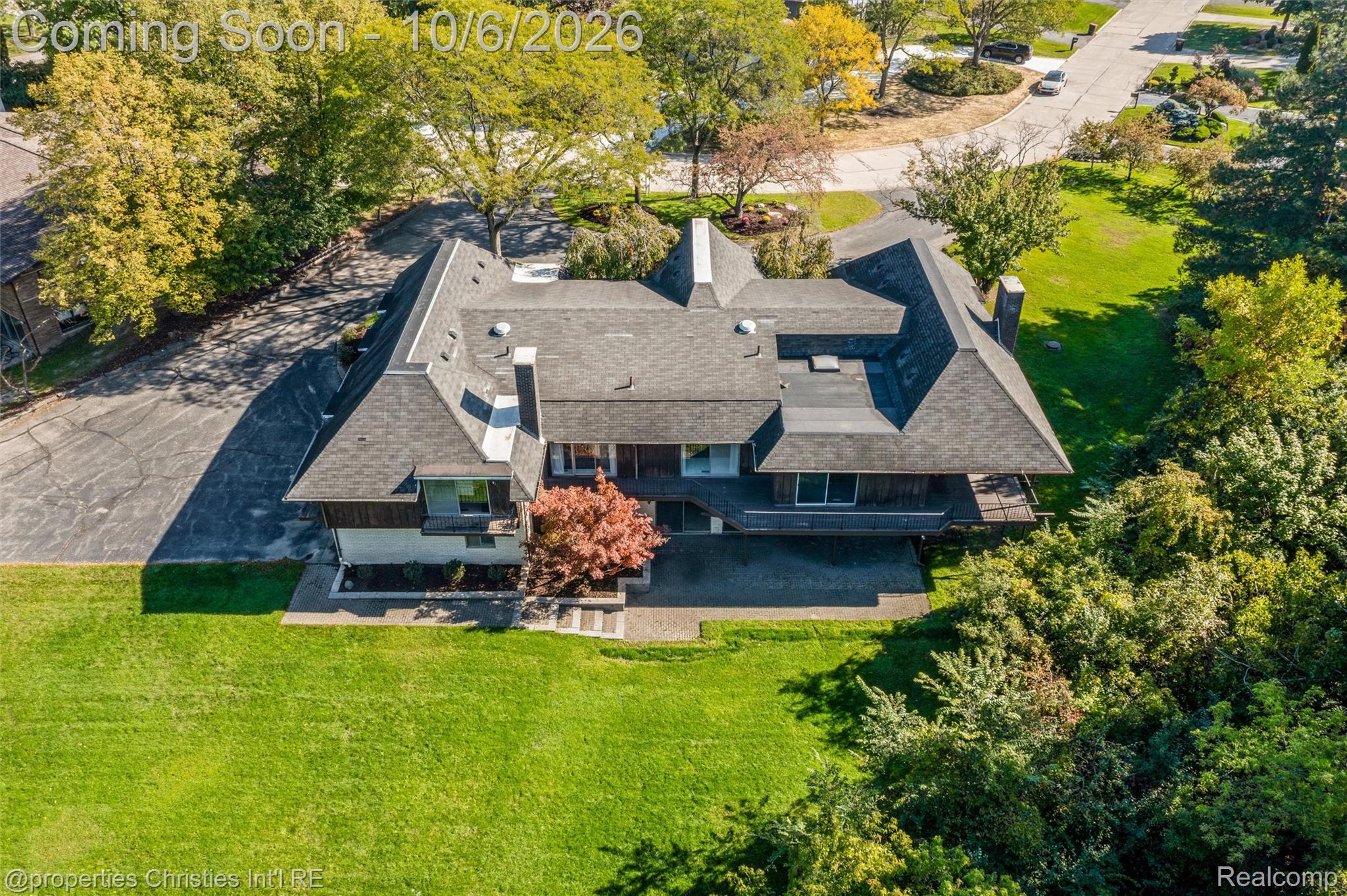 Aerial view of a large house with a complex roof, wraparound deck, and expansive lawn.