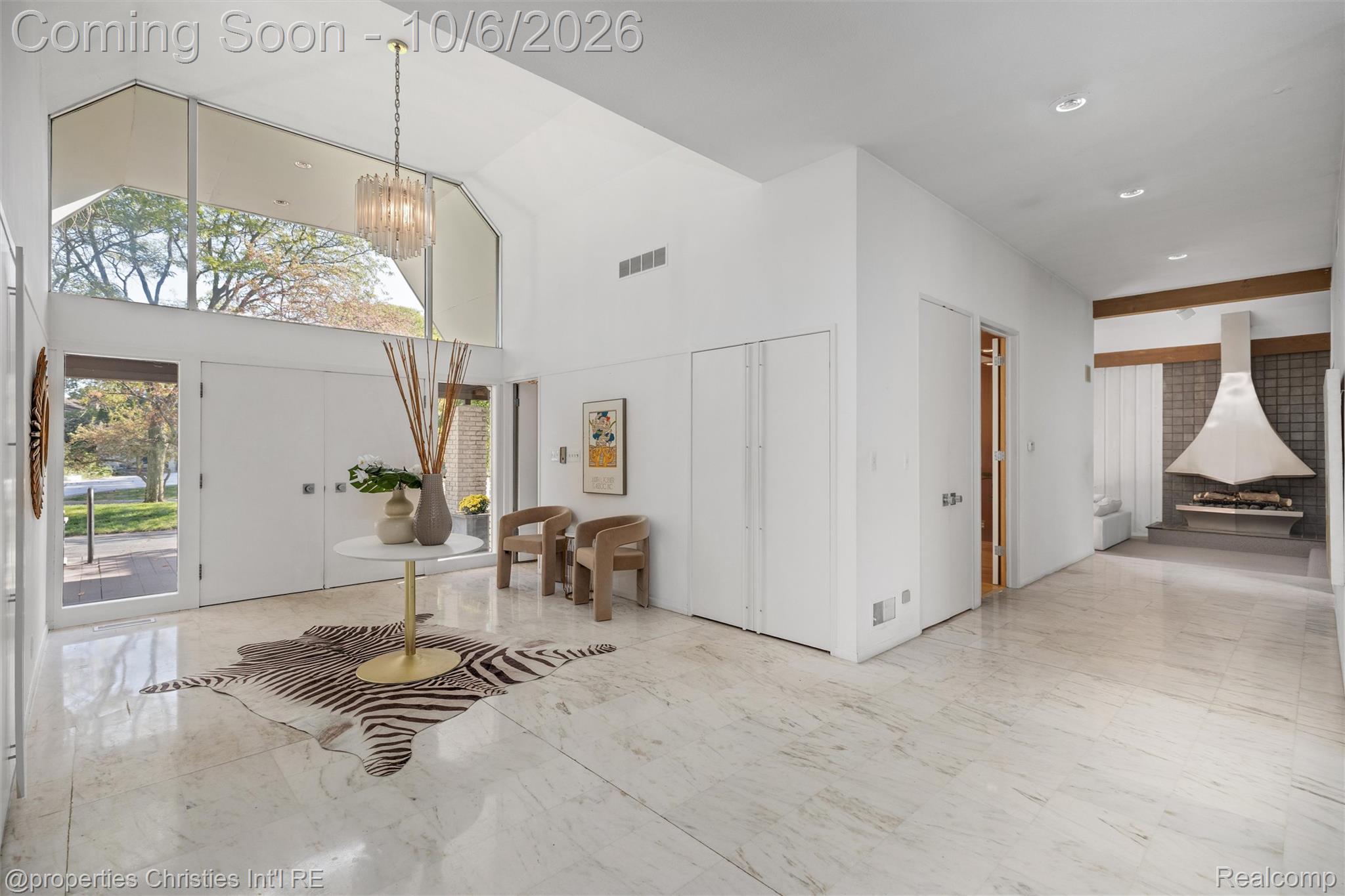 Furnished entry hall with vaulted ceiling, marble floors, large windows, and a sculptural fireplace in the adjoining room.
