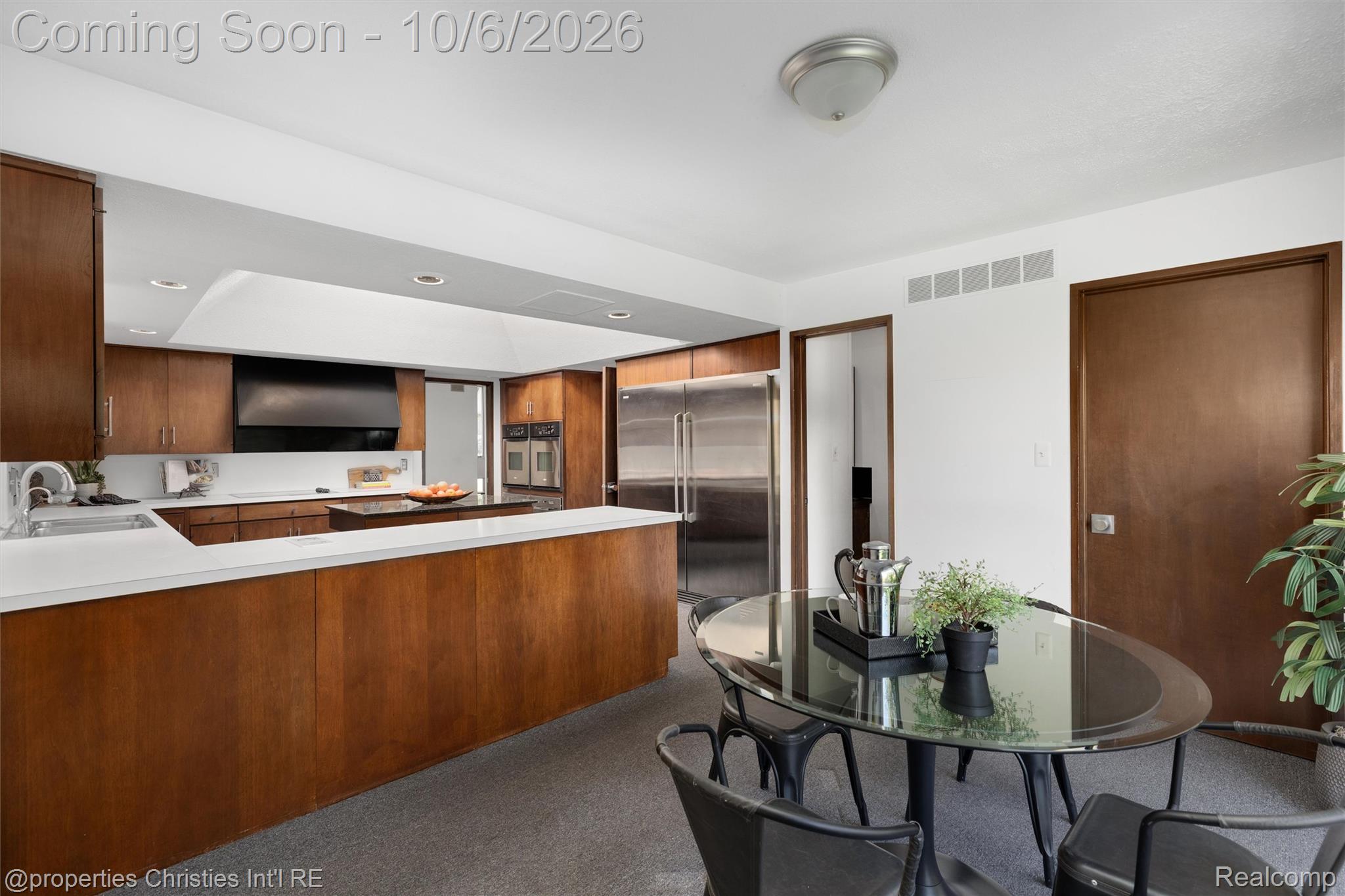 Kitchen and dining area with warm wood cabinets, stainless appliances, and a glass table.