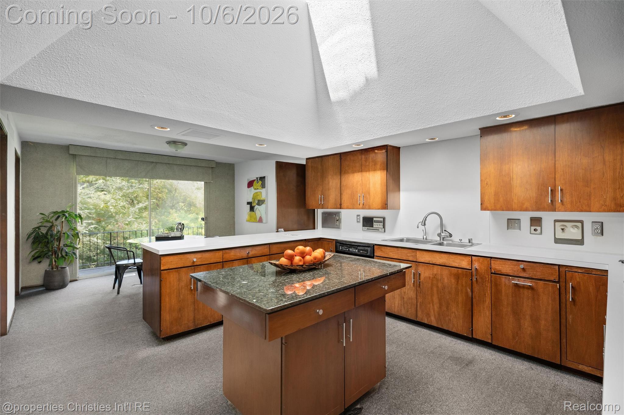 Kitchen with wood cabinetry, granite island, and large window beneath a vaulted skylight.