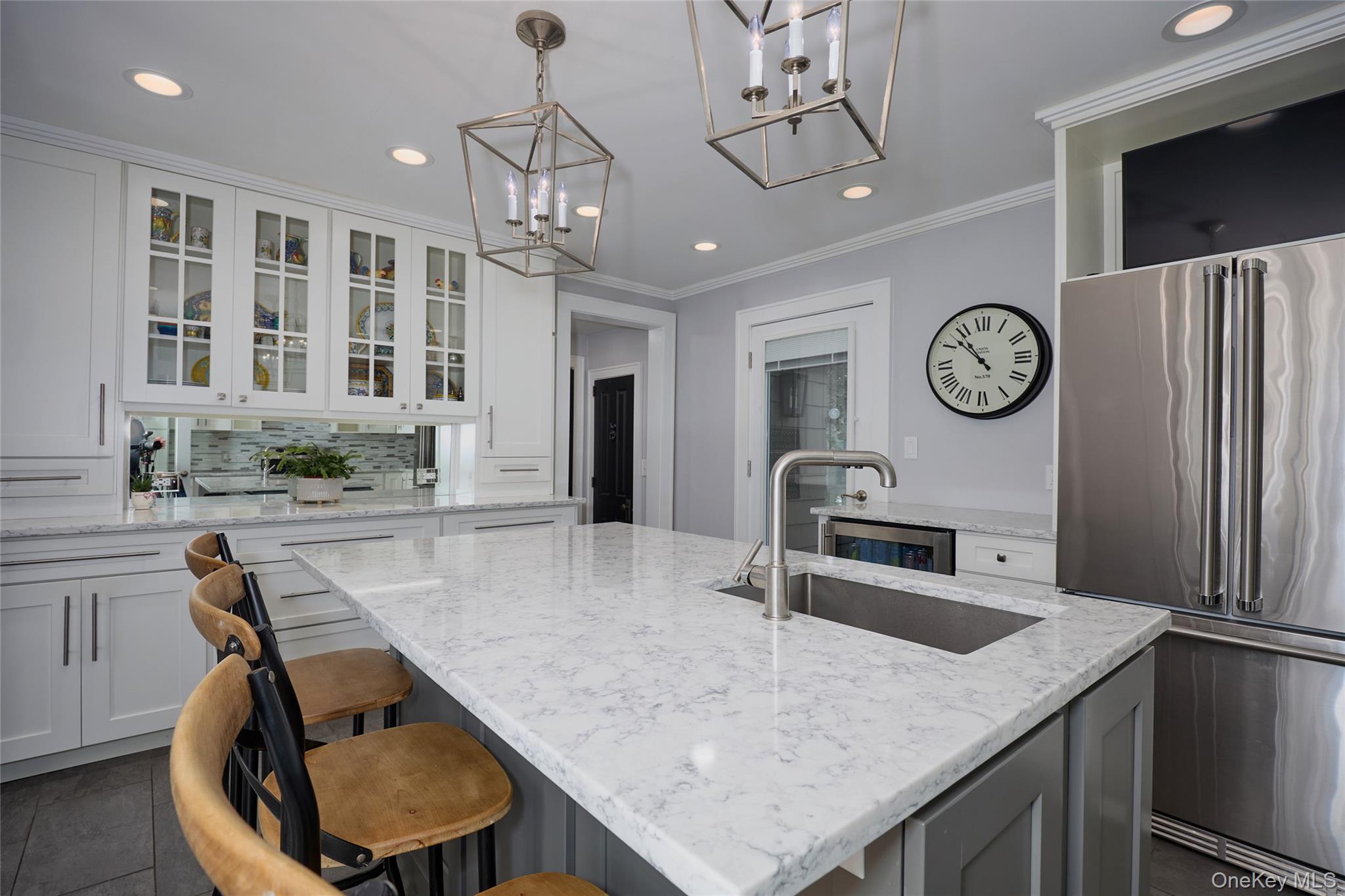 Kitchen with a large marble island, glass-front cabinets, and stainless steel refrigerator.