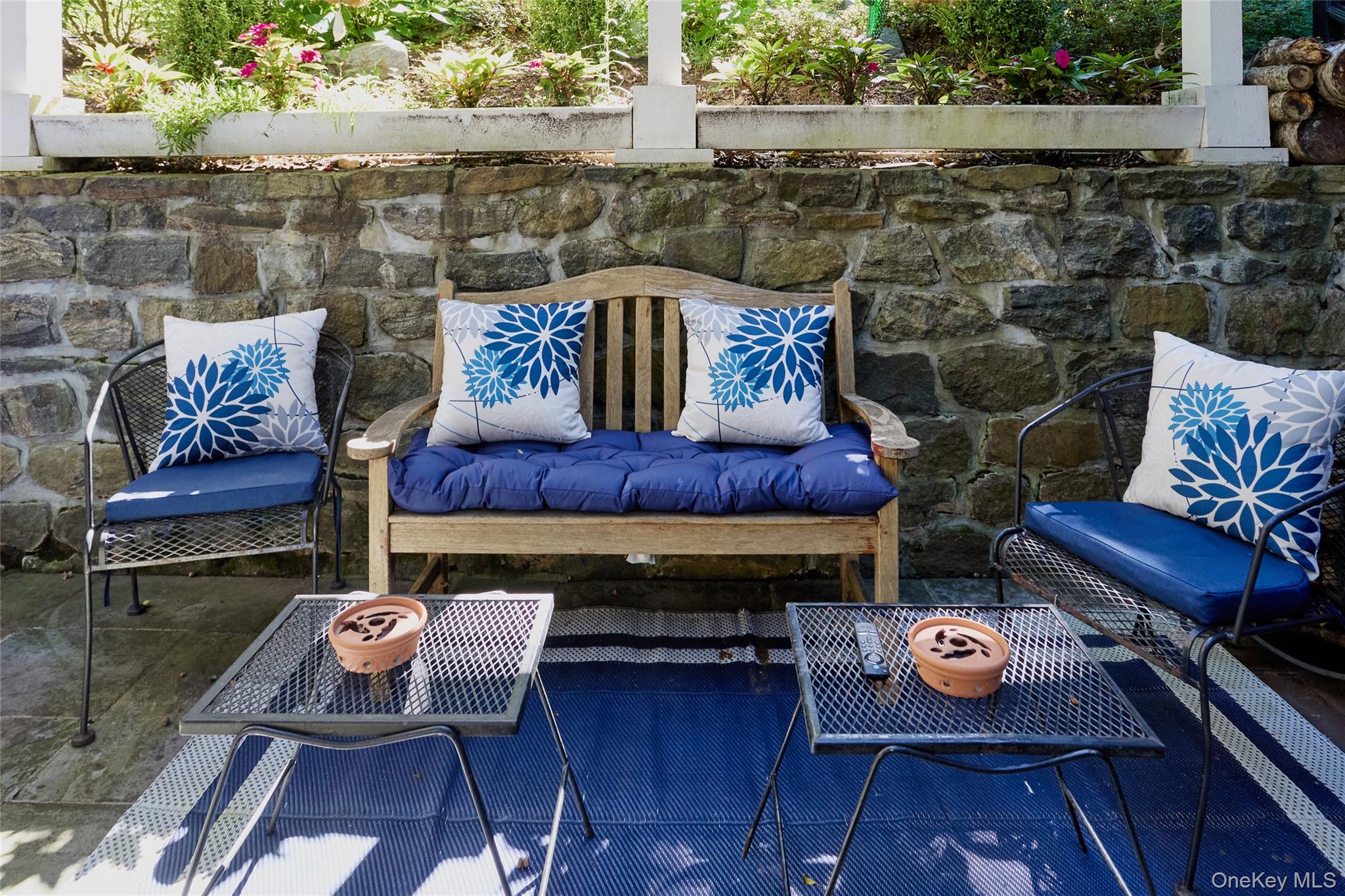 Outdoor patio seating with blue cushions and patterned pillows against a stone retaining wall.
