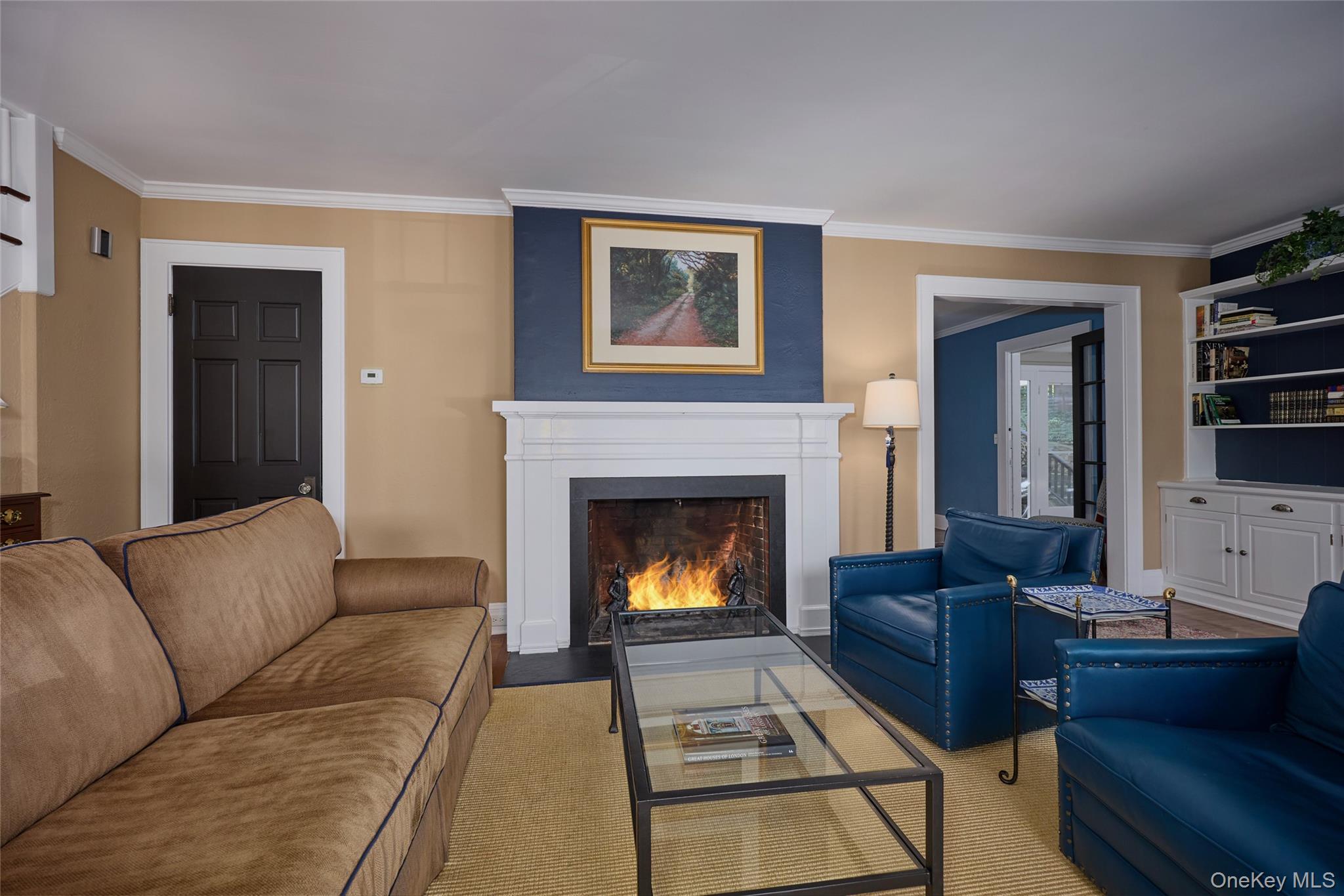 Living room with a lit fireplace, tan sofa, and blue leather armchairs.