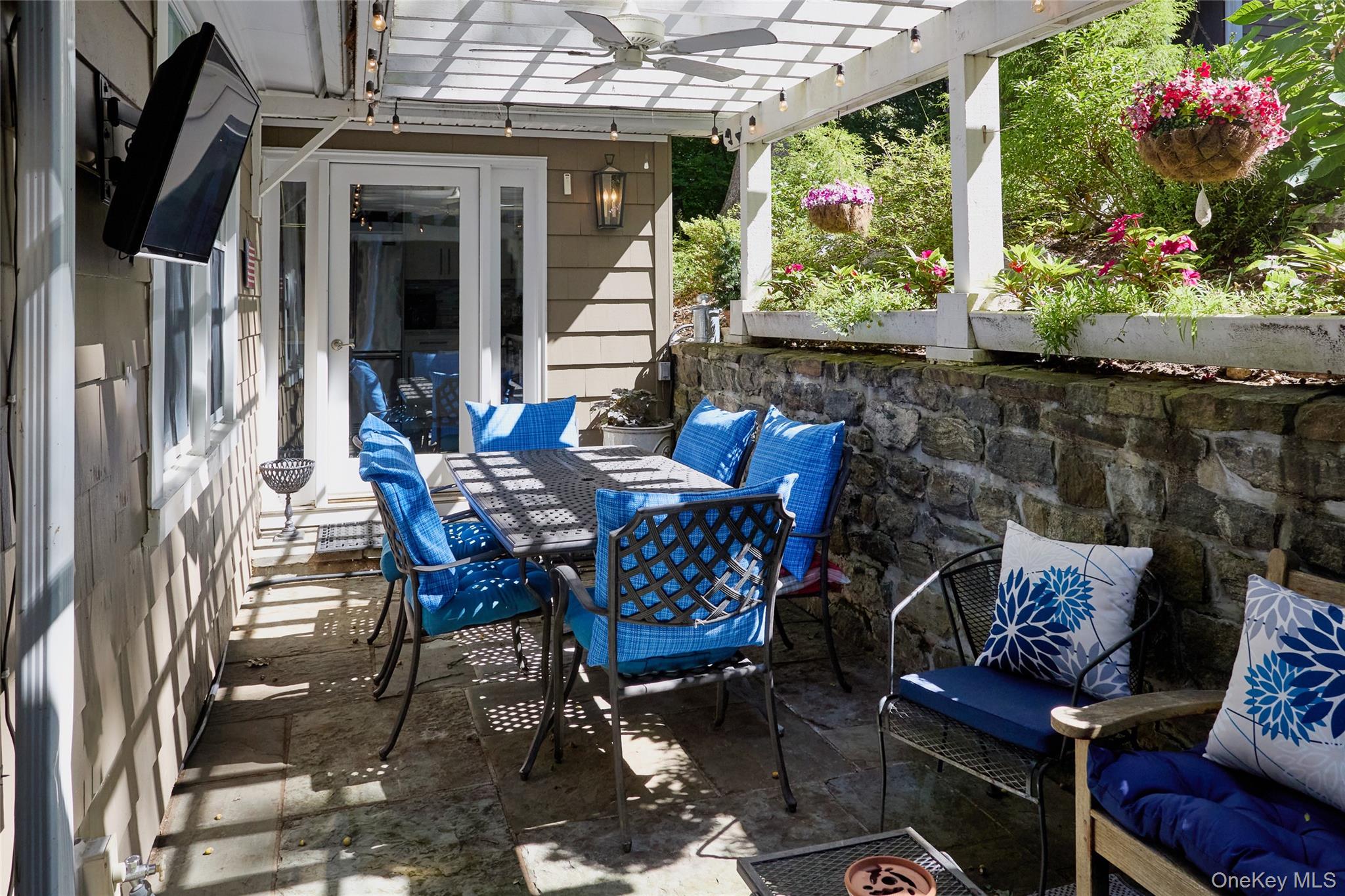 Furnished stone patio with a white pergola, blue-cushioned dining set, and flower baskets.