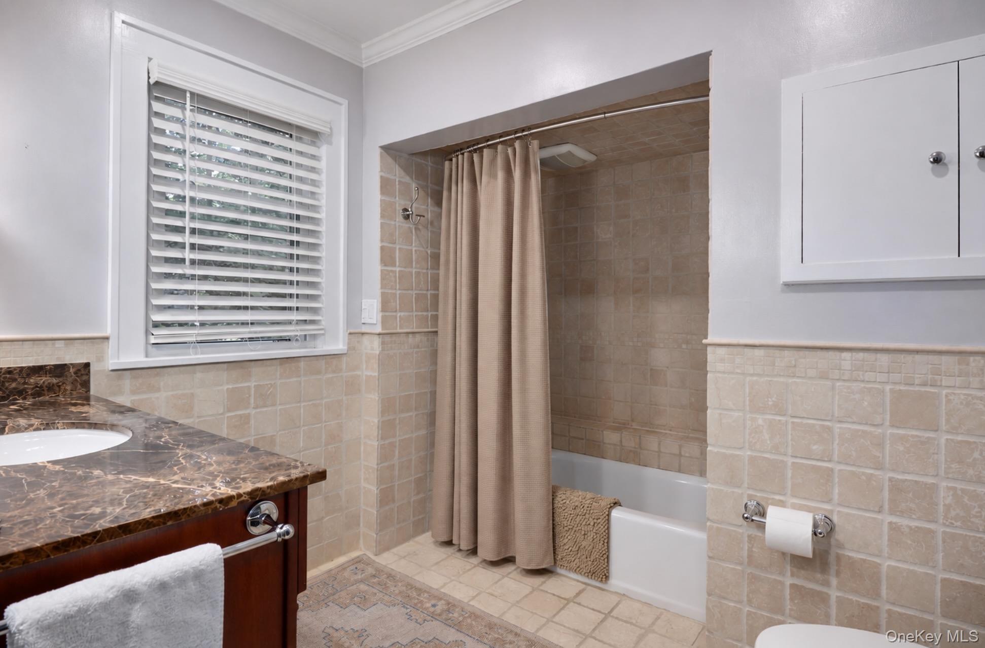 Bathroom with beige tiled tub and shower, marble-look vanity, and a window with white blinds.