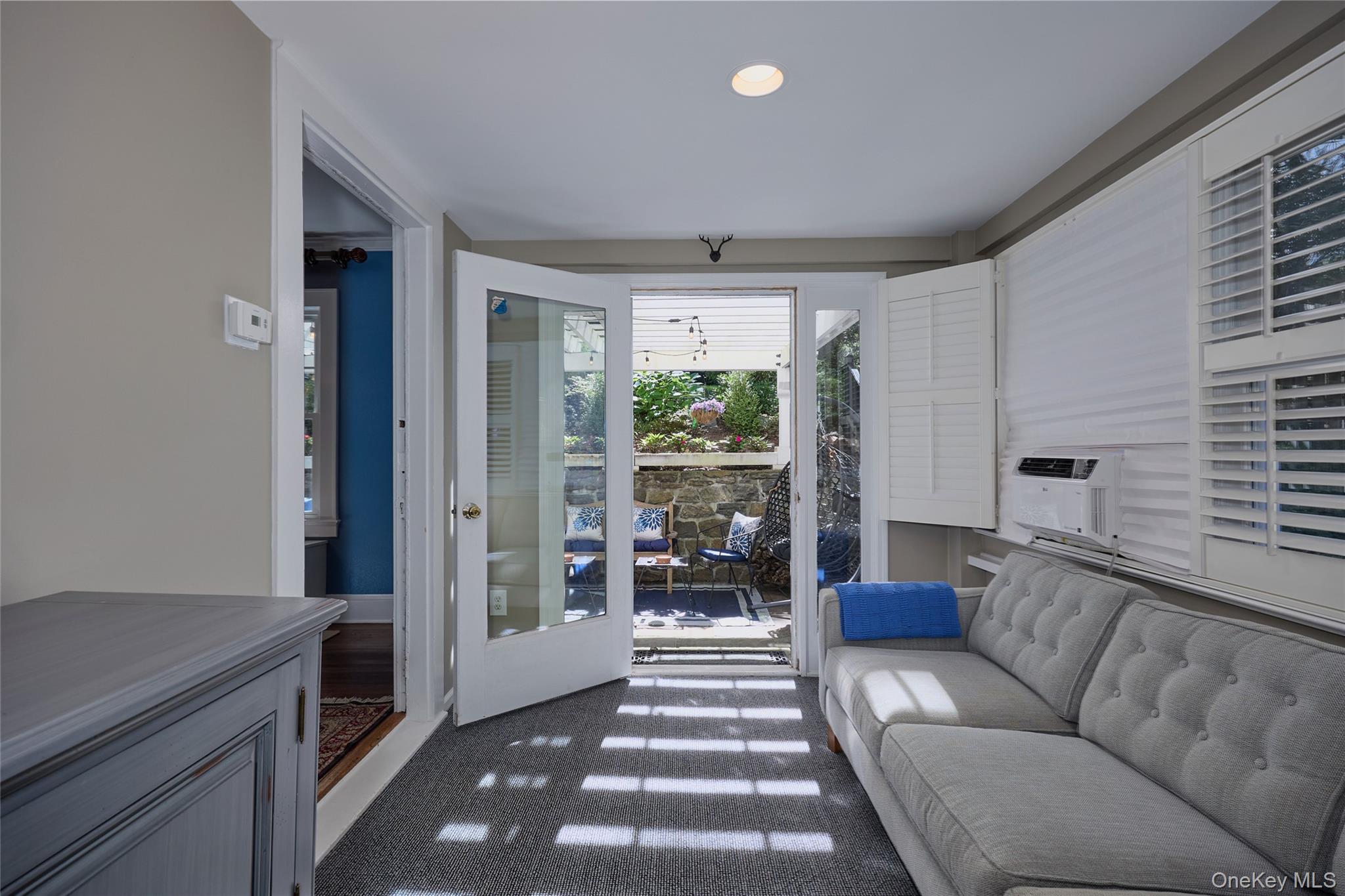 Furnished sitting room with a gray sofa and open doors to a garden patio.