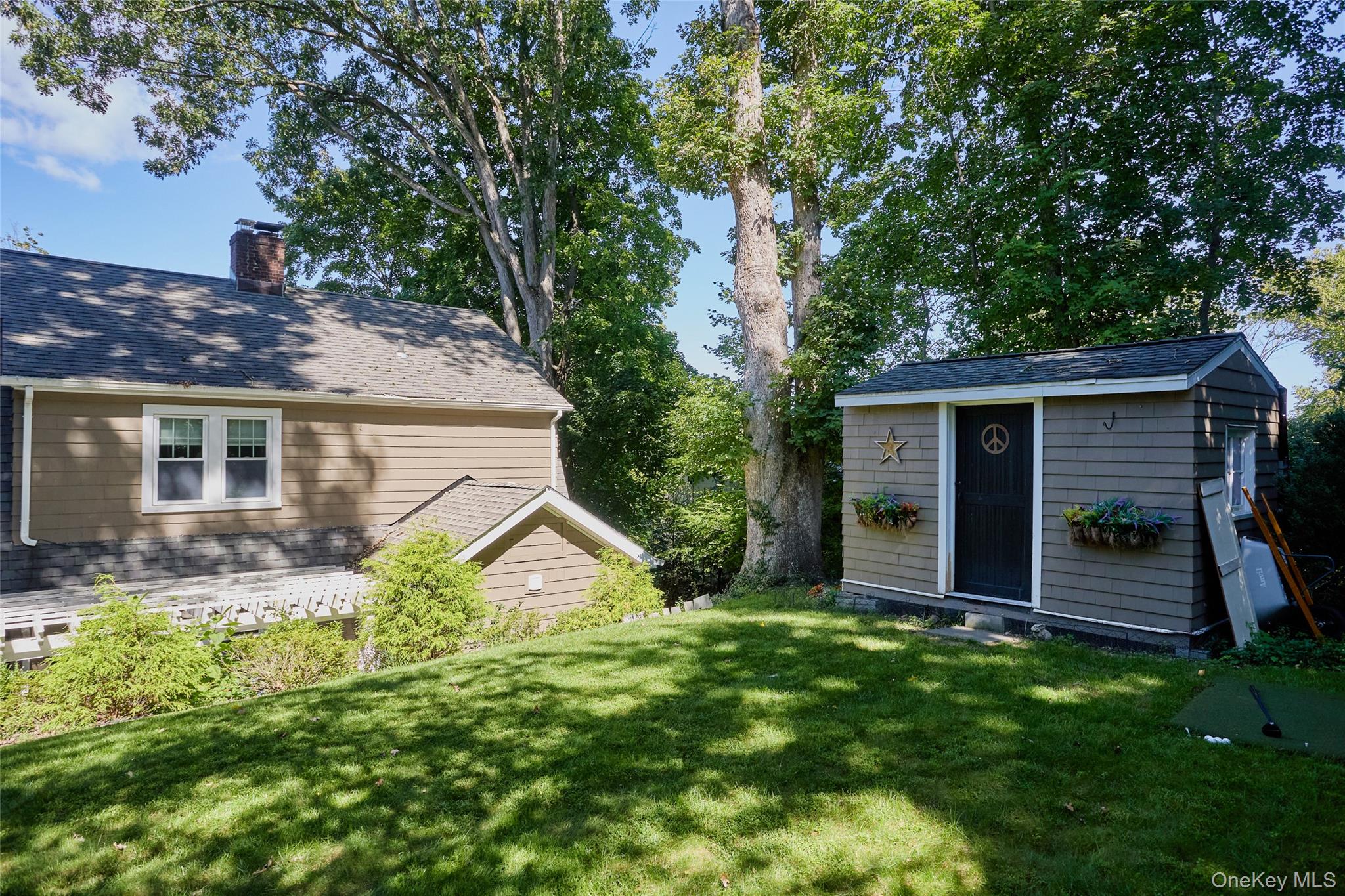 Tree-shaded lawn beside a brown house and gray shed with flower boxes.