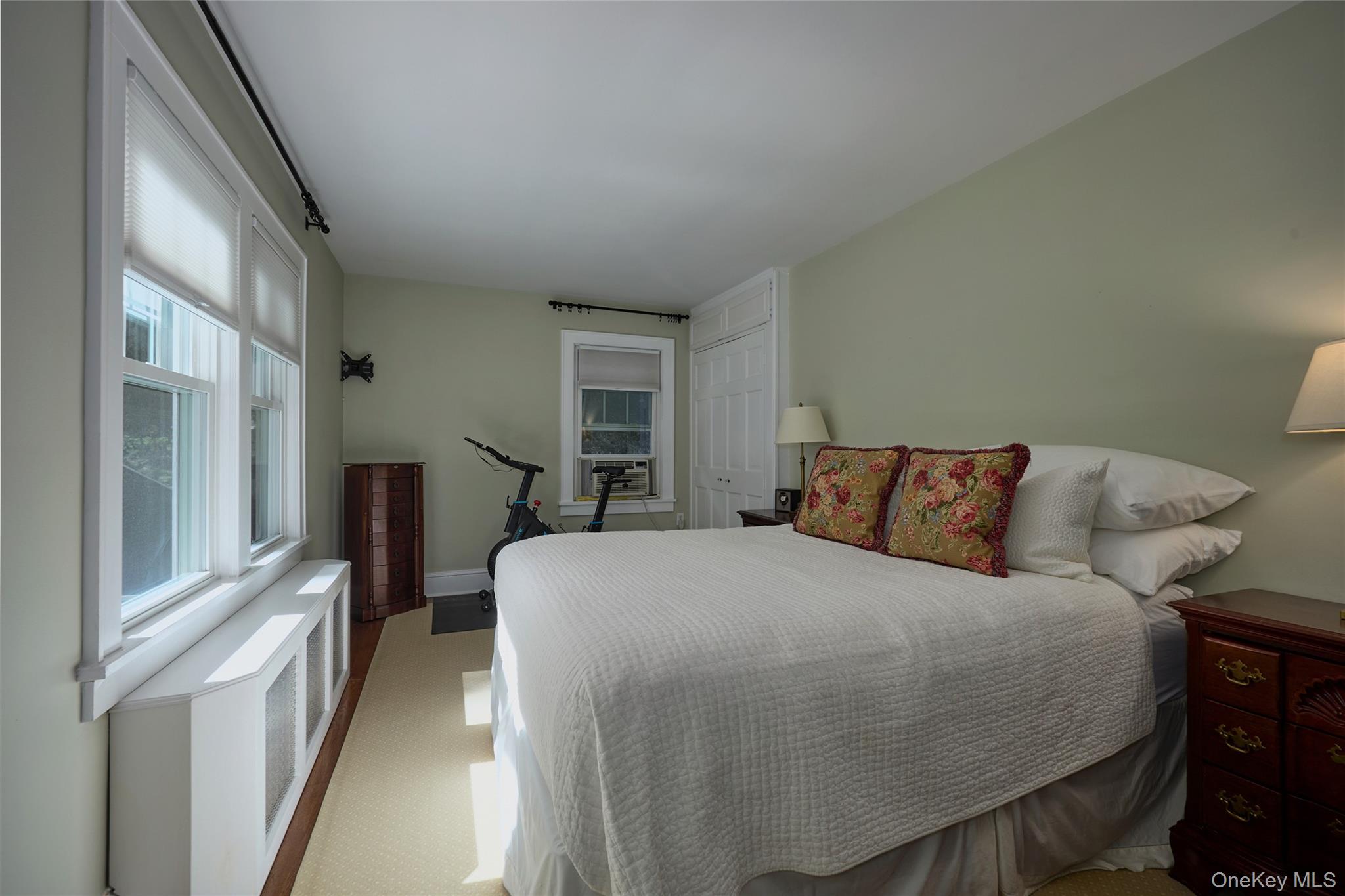 Furnished bedroom with a large white bed, tall windows, and an exercise bike.
