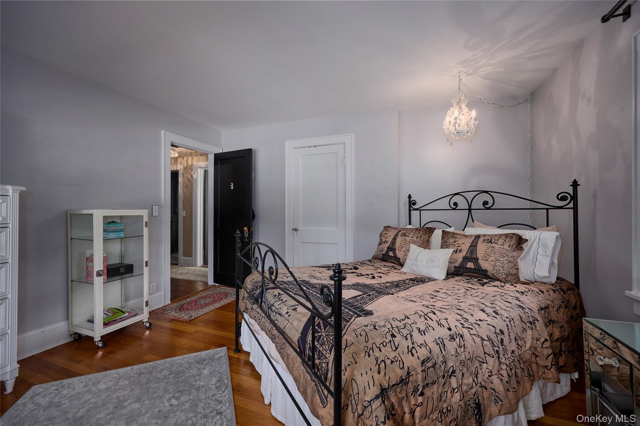 Bedroom with a wrought-iron bed, Paris-themed bedding, hardwood floors, and a hanging crystal chandelier.