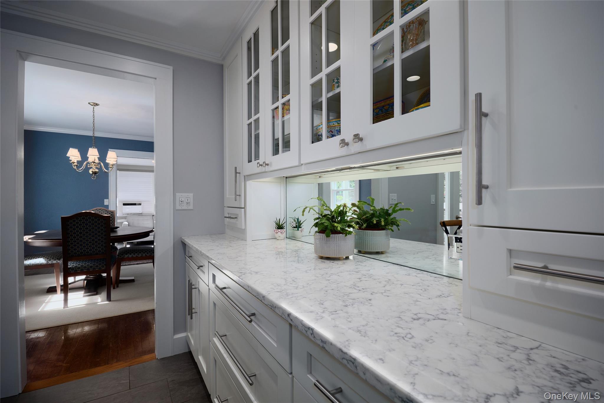 White kitchen with glass-front cabinets, a long marble countertop, and a view into the dining room.