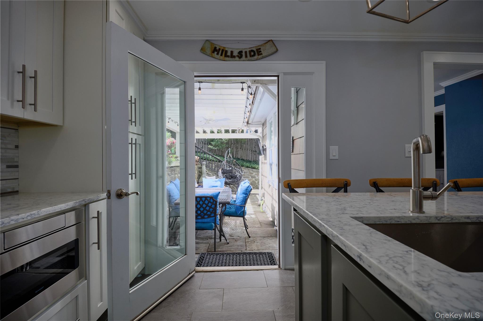 Kitchen with white cabinets and marble counters opening onto a covered patio with blue seating.