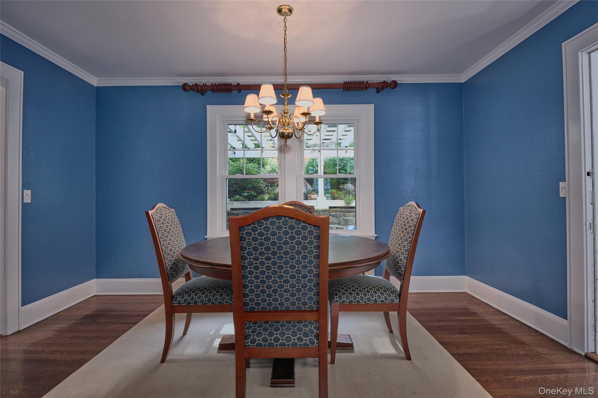 Dining room with blue walls, a round wooden table, patterned chairs, and a brass chandelier.