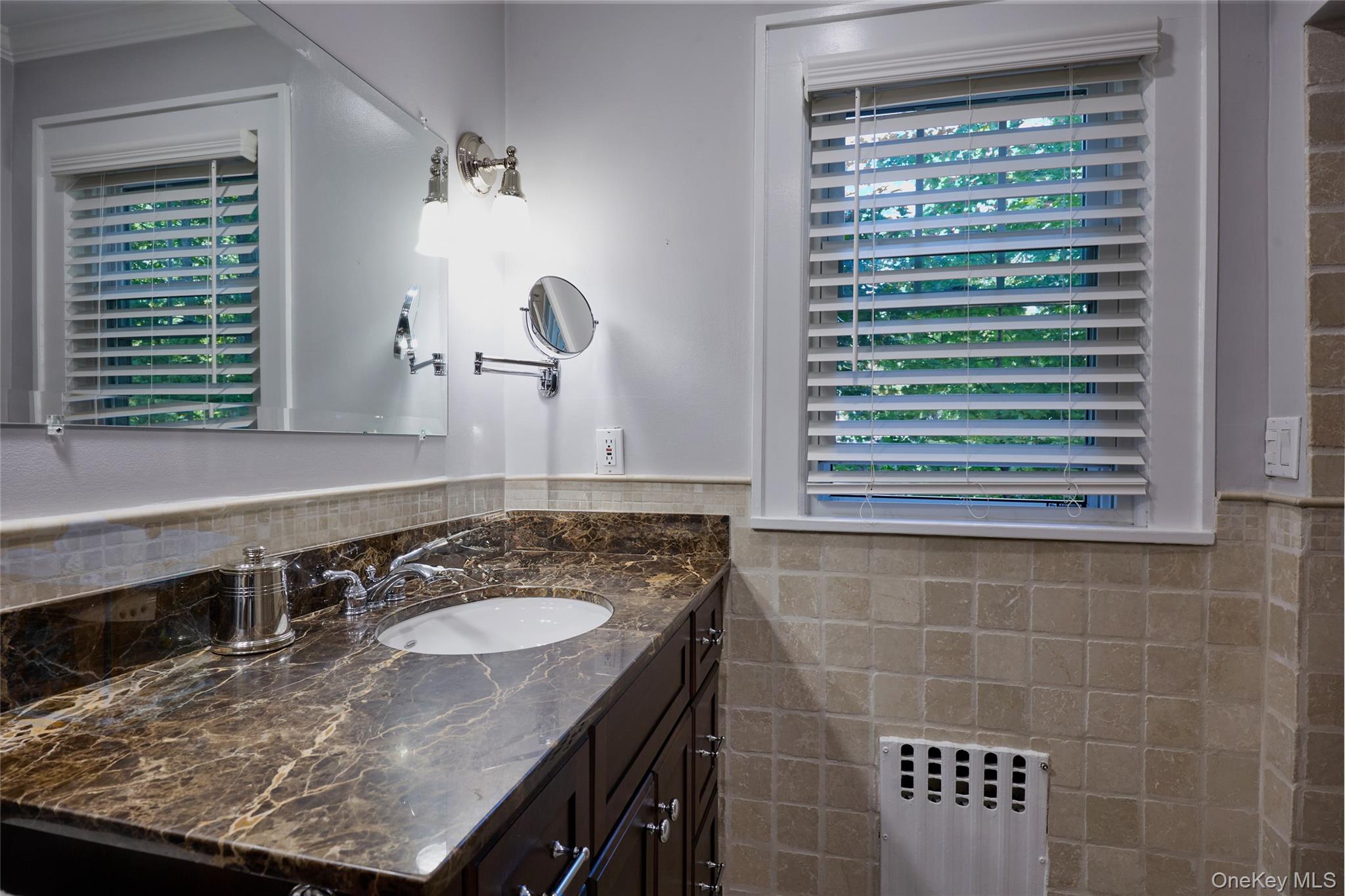 Bathroom with a veined marble vanity, inset sink, and window with white blinds.