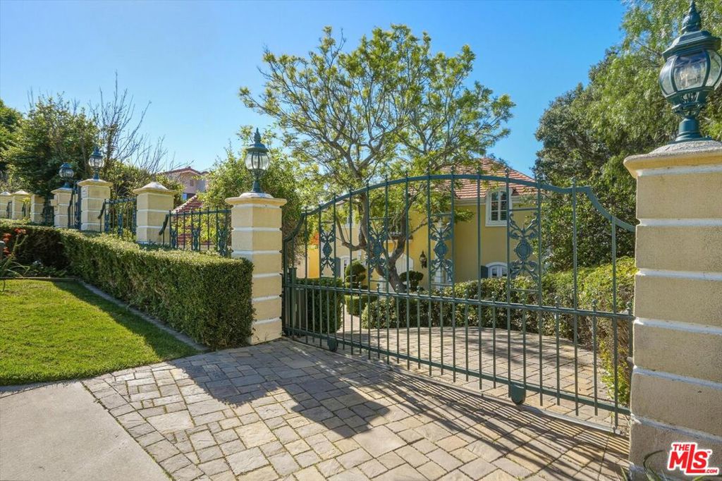 Yellow two-story home behind an ornate metal gate and cream masonry pillars.