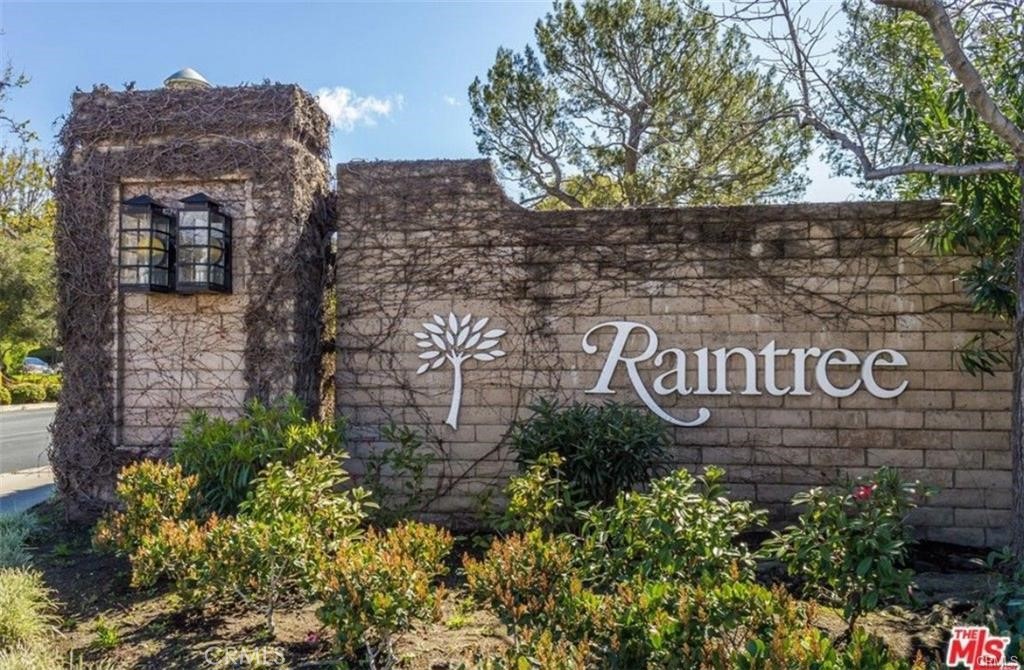 Raintree community entrance sign on a vine-covered stone wall with landscaping.