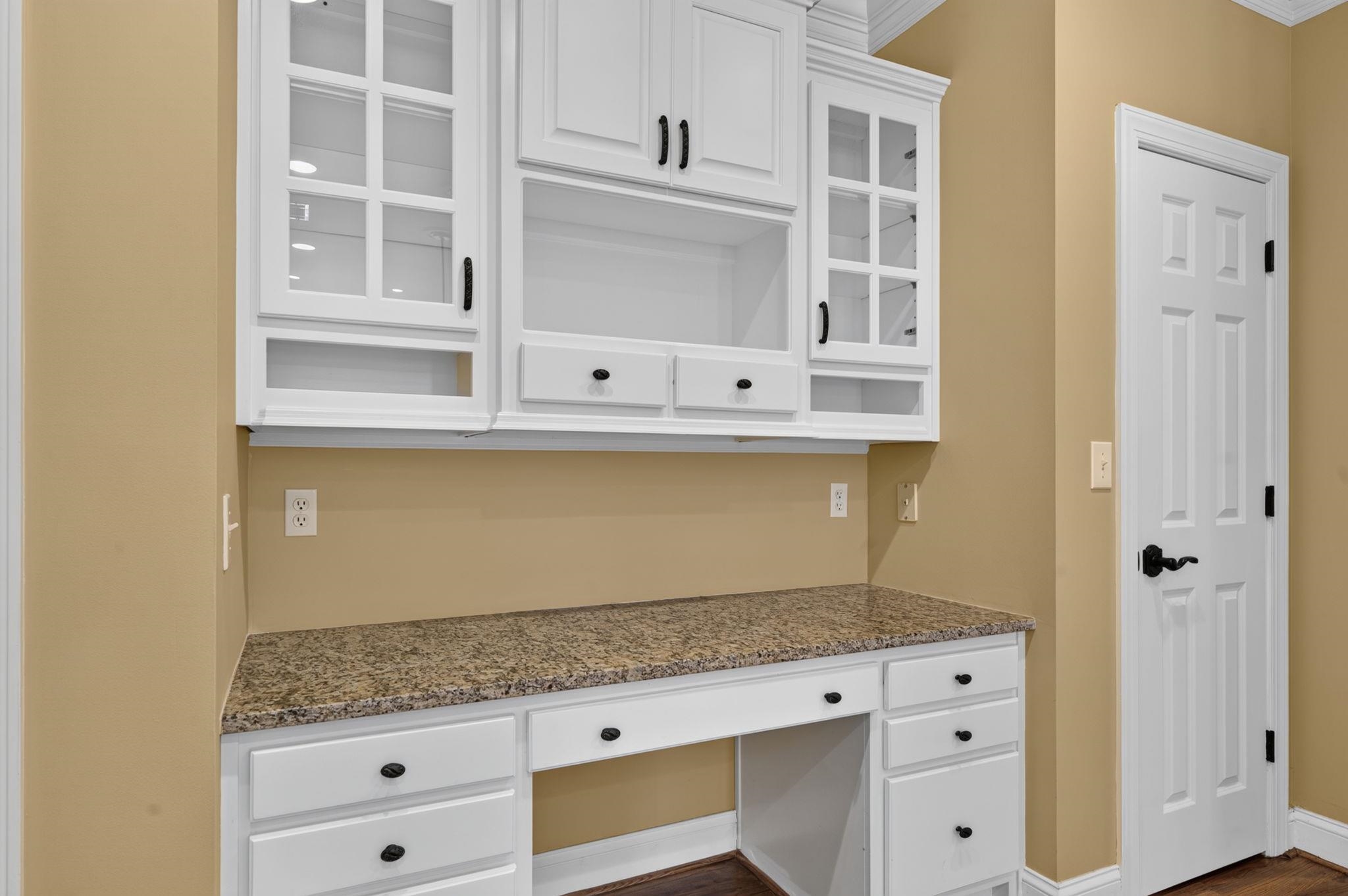 Built-in pantry work area with white cabinets, glass-front cupboards, and a granite countertop.